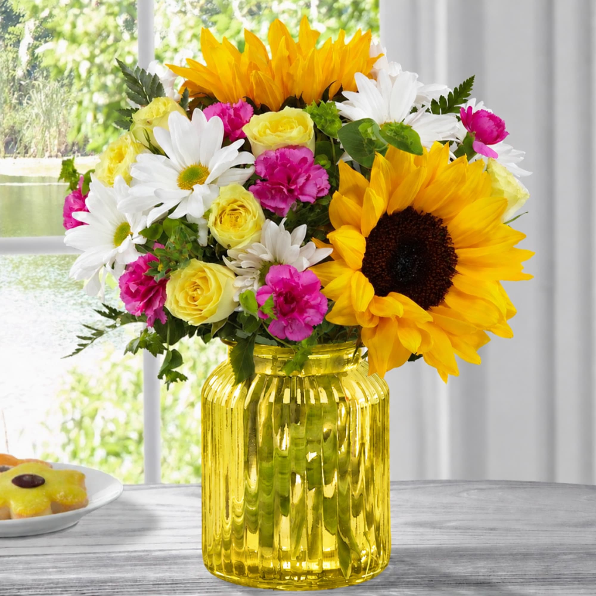 Bouquet of sunflowers, white daisies, yellow roses, and pink carnations in a yellow glass vase