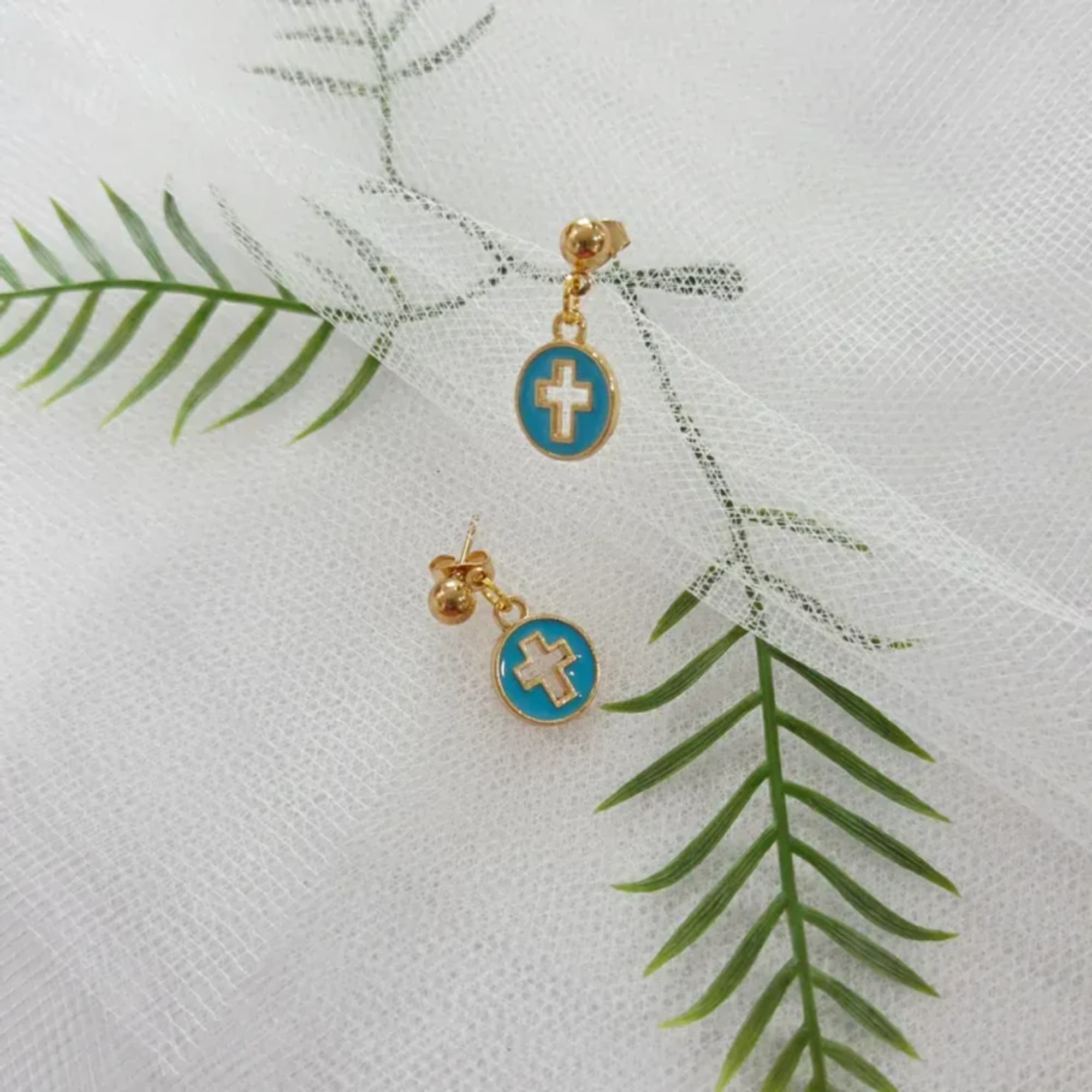 Pair of blue cross earrings on white mesh fabric with green fern leaves
