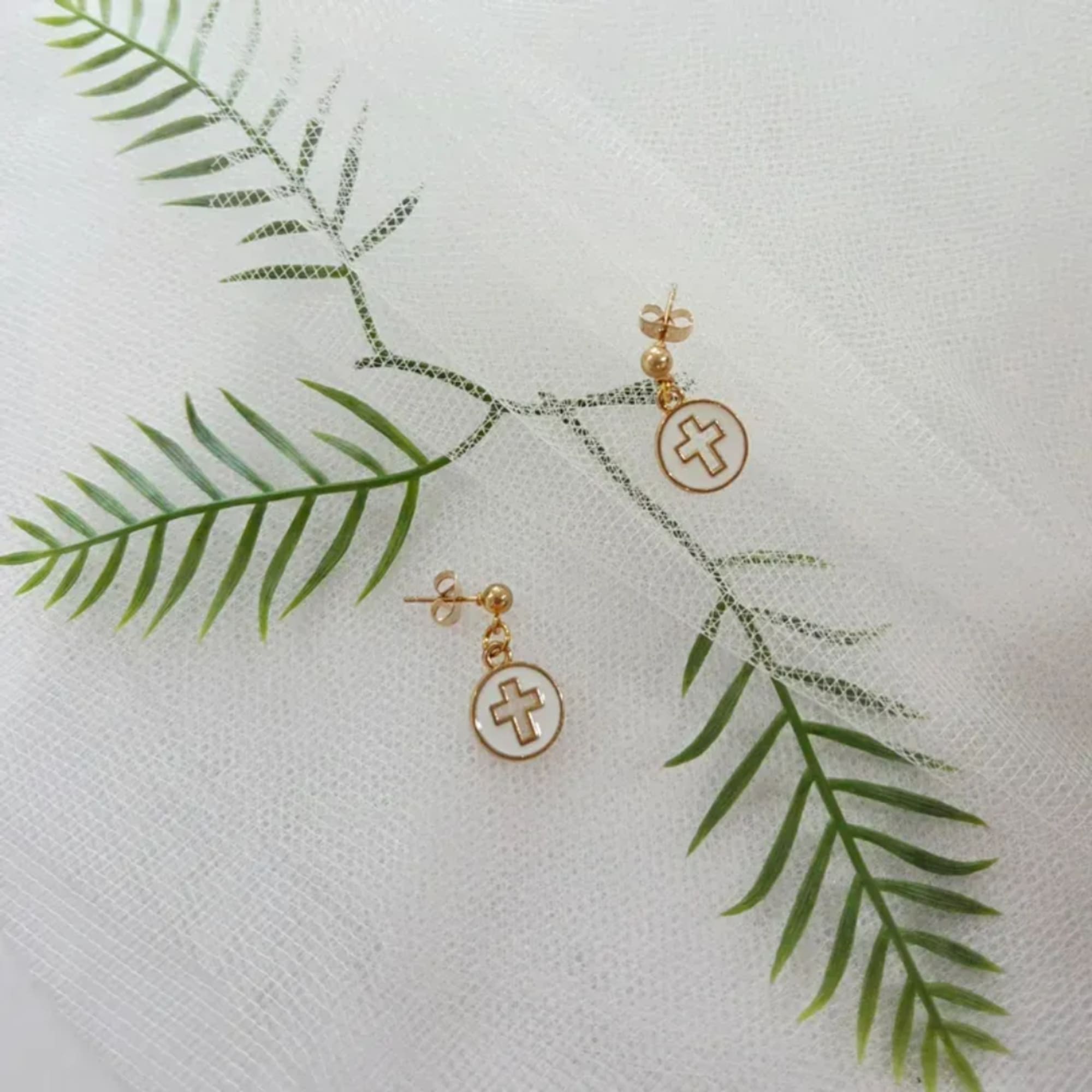 Gold cross earrings on a white textured fabric background