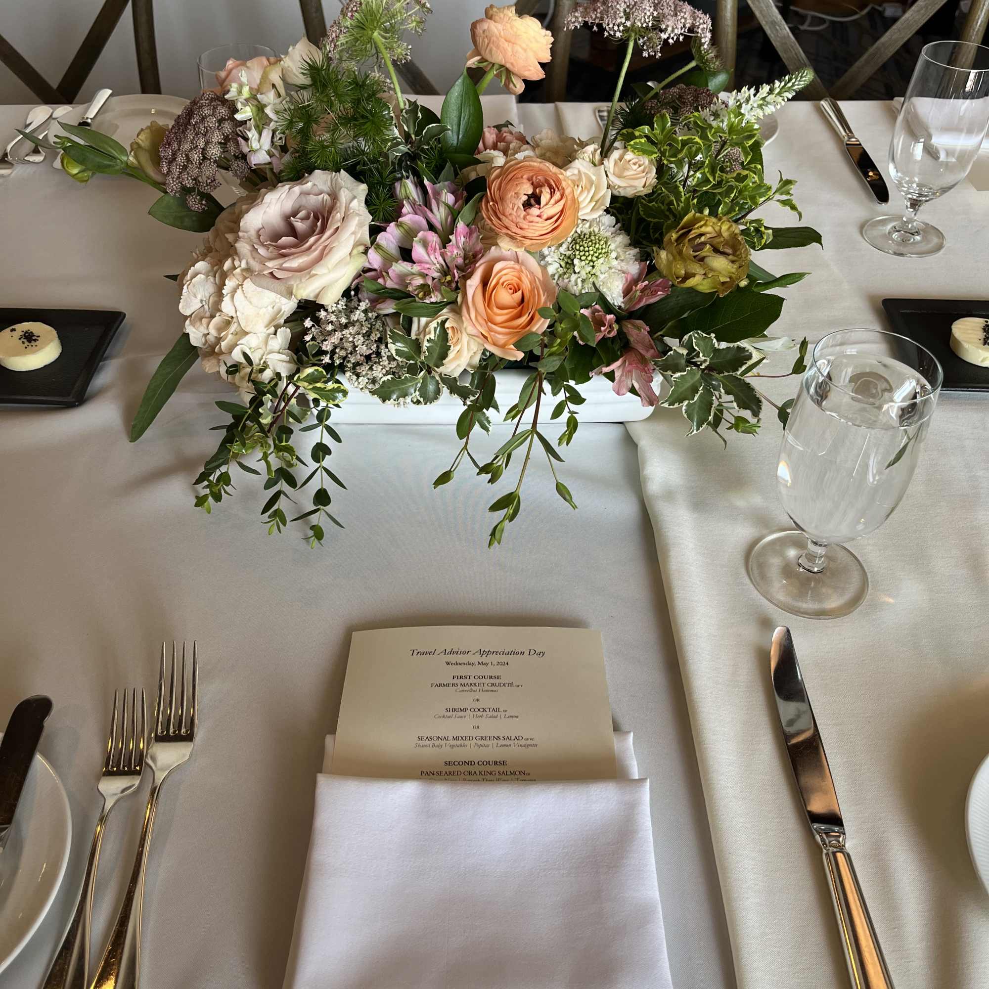 Low floral centerpiece with peach, blush, and white blooms on a dining table