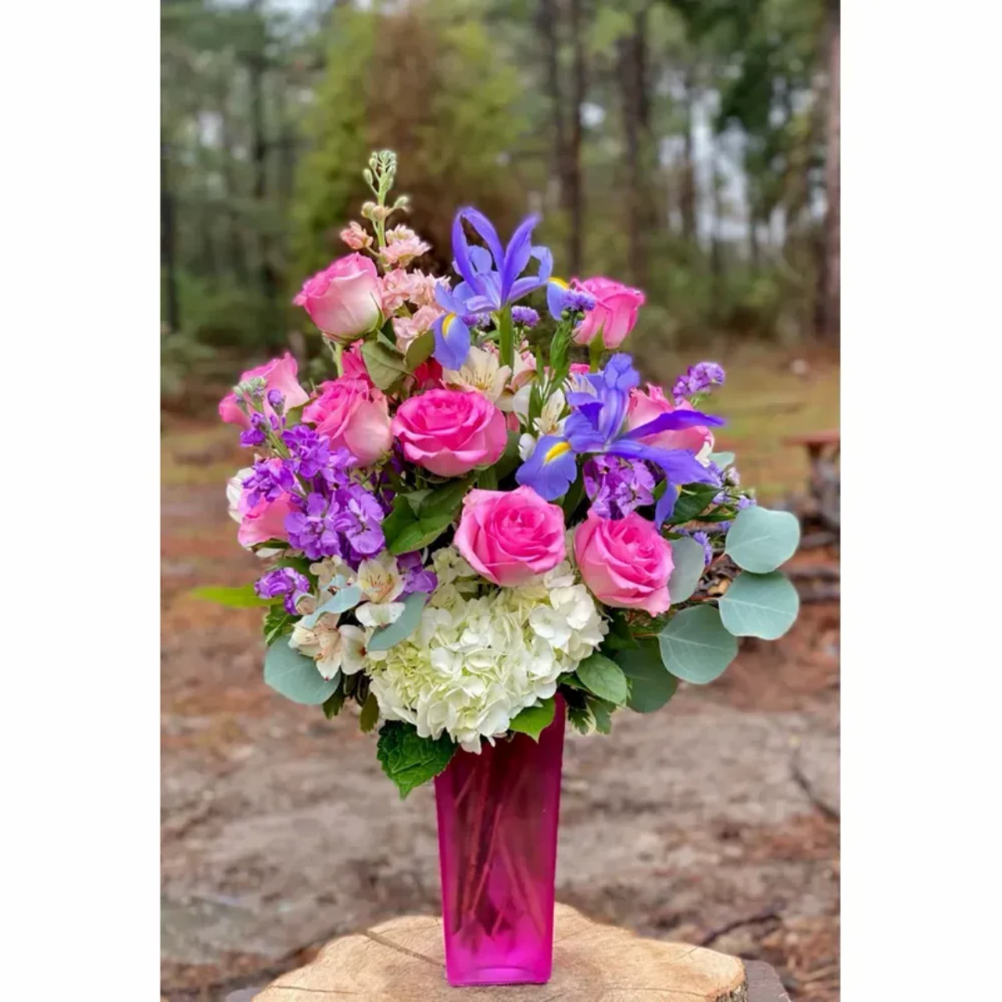 Pink roses and purple flowers arranged in a tall magenta vase