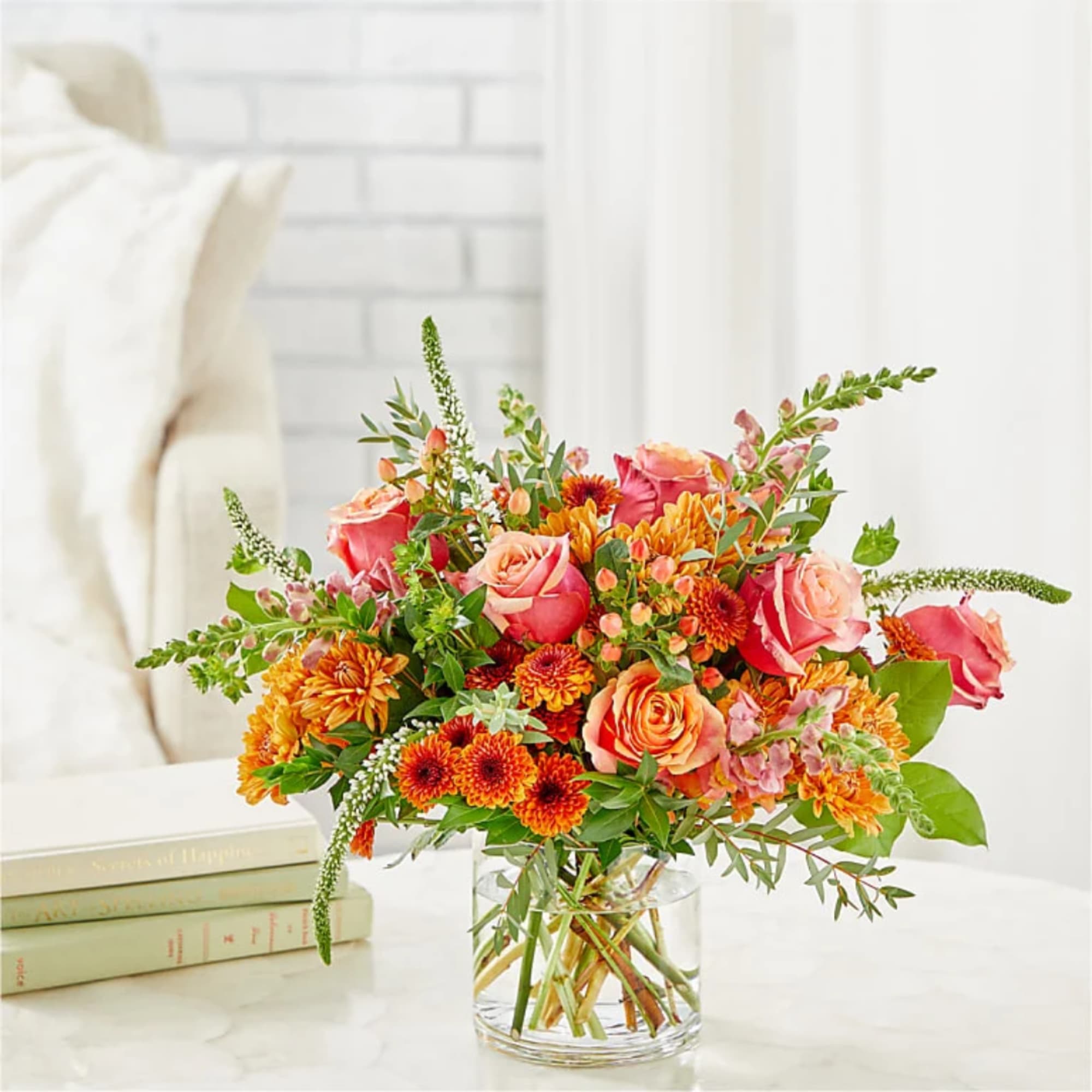 Mixed bouquet of pink roses and orange flowers in a clear glass vase