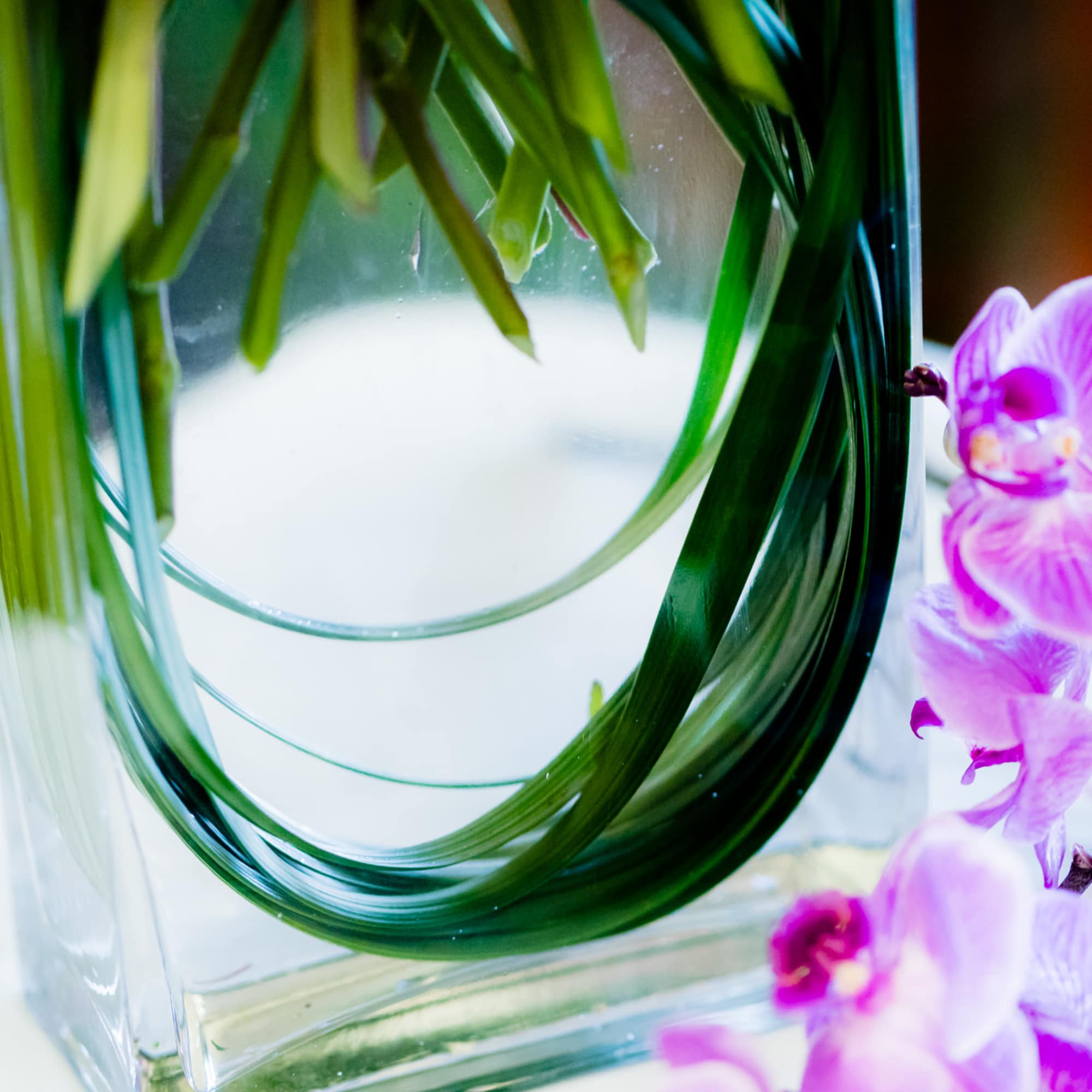 Purple orchids beside a clear glass vase with long green leaves