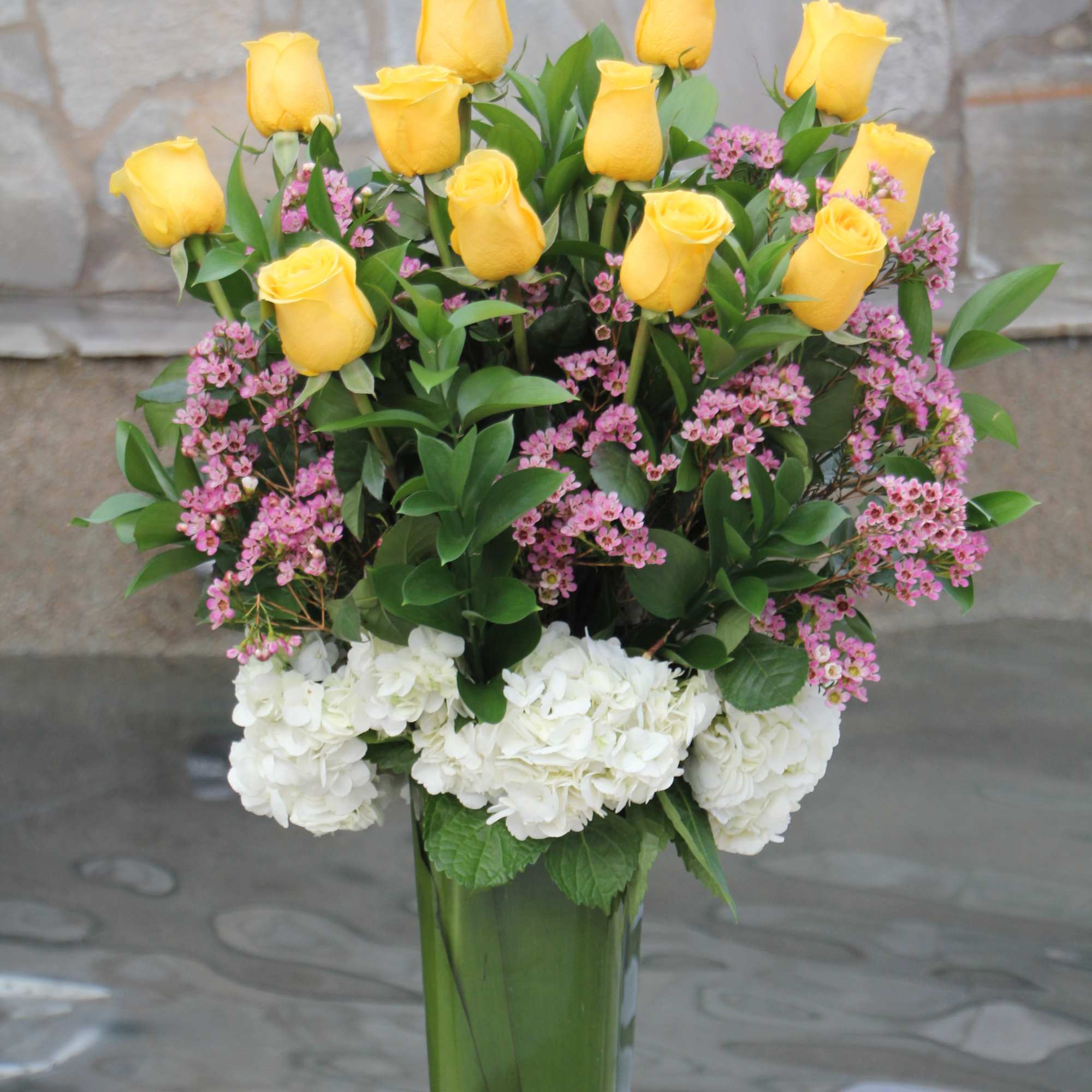 Yellow roses and pink flowers in a tall glass vase