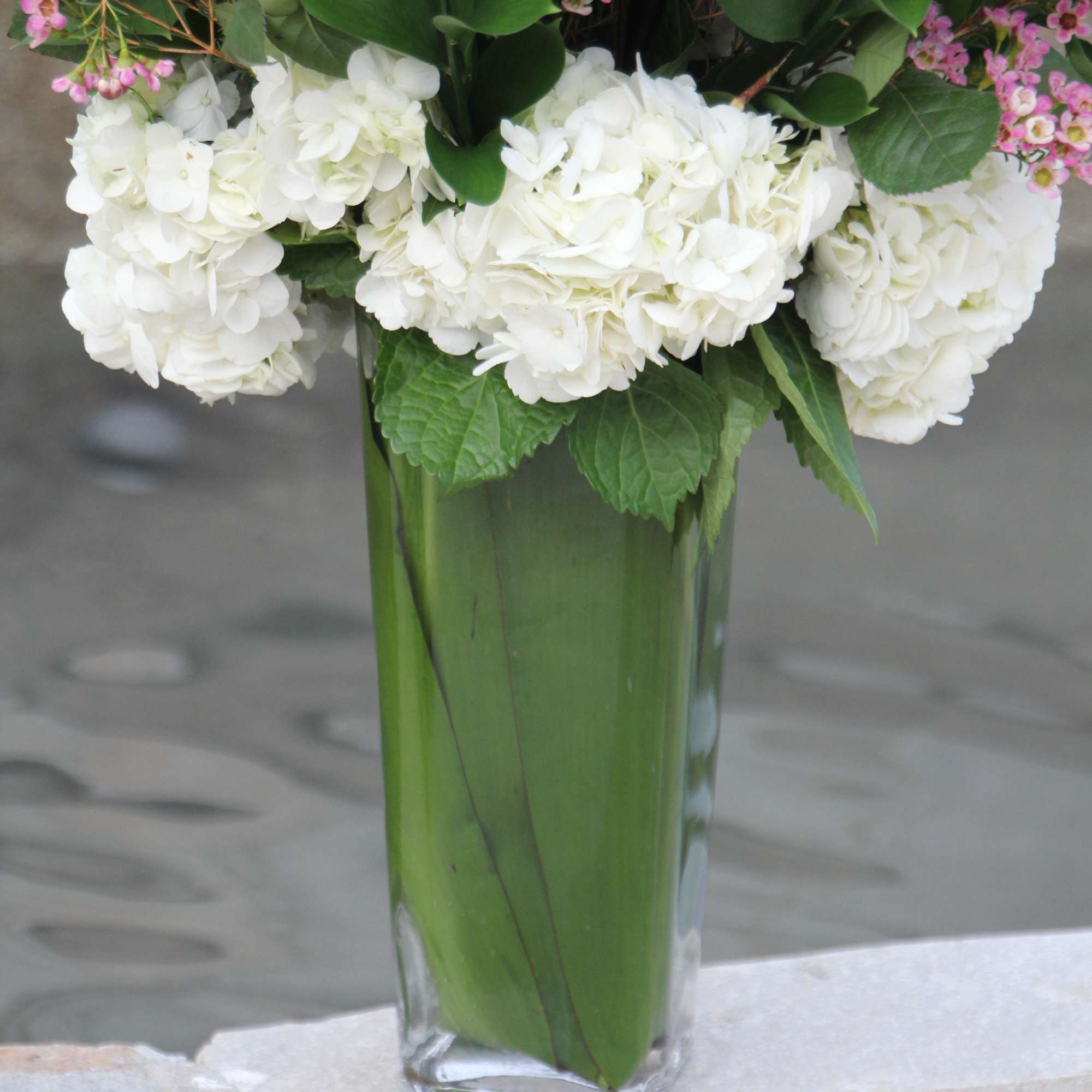 White hydrangeas and pink filler flowers in a tall glass vase