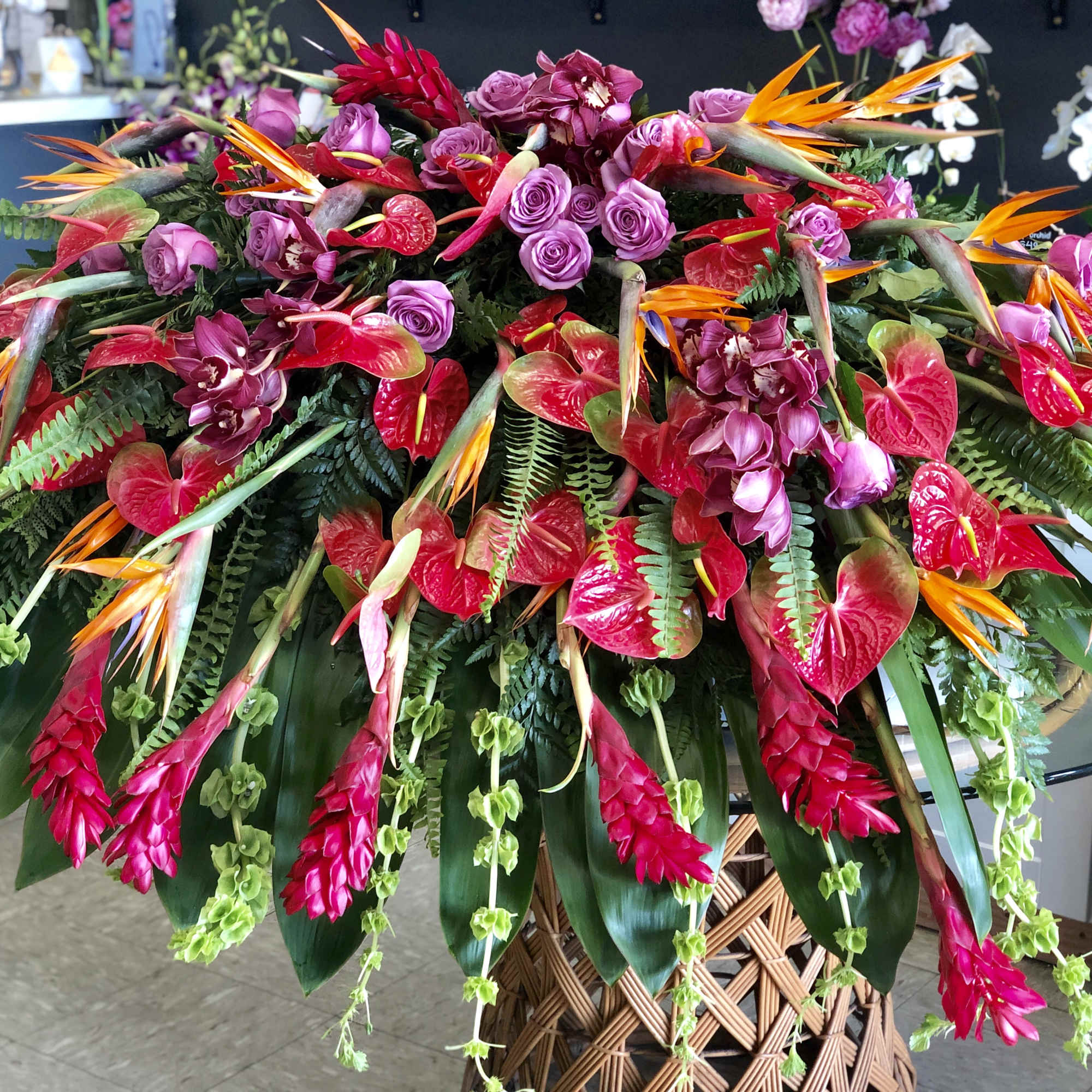 Large tropical floral arrangement with red, pink, and orange blooms in a woven basket
