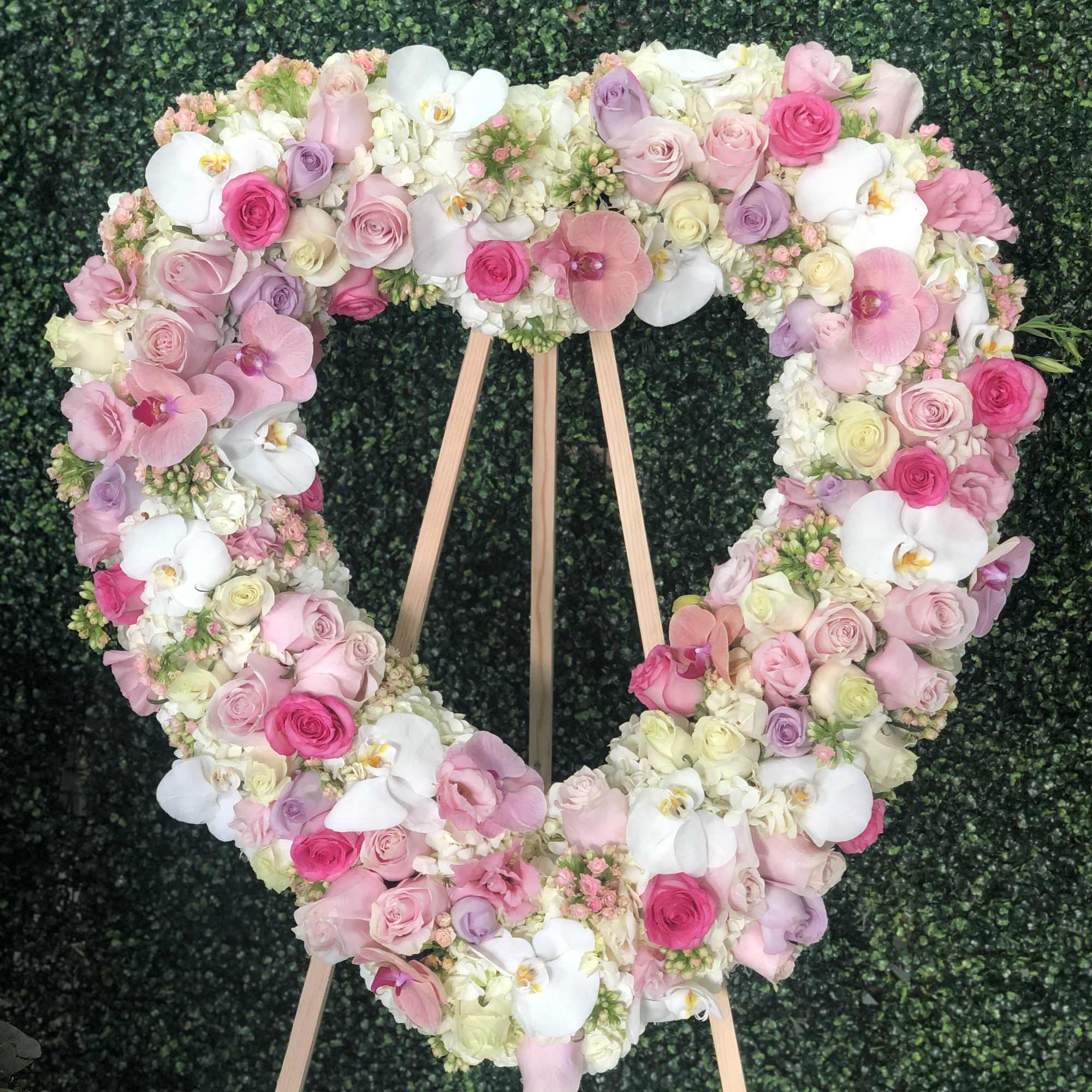 Heart-shaped floral wreath of pink, white, and lavender blooms on a wooden stand