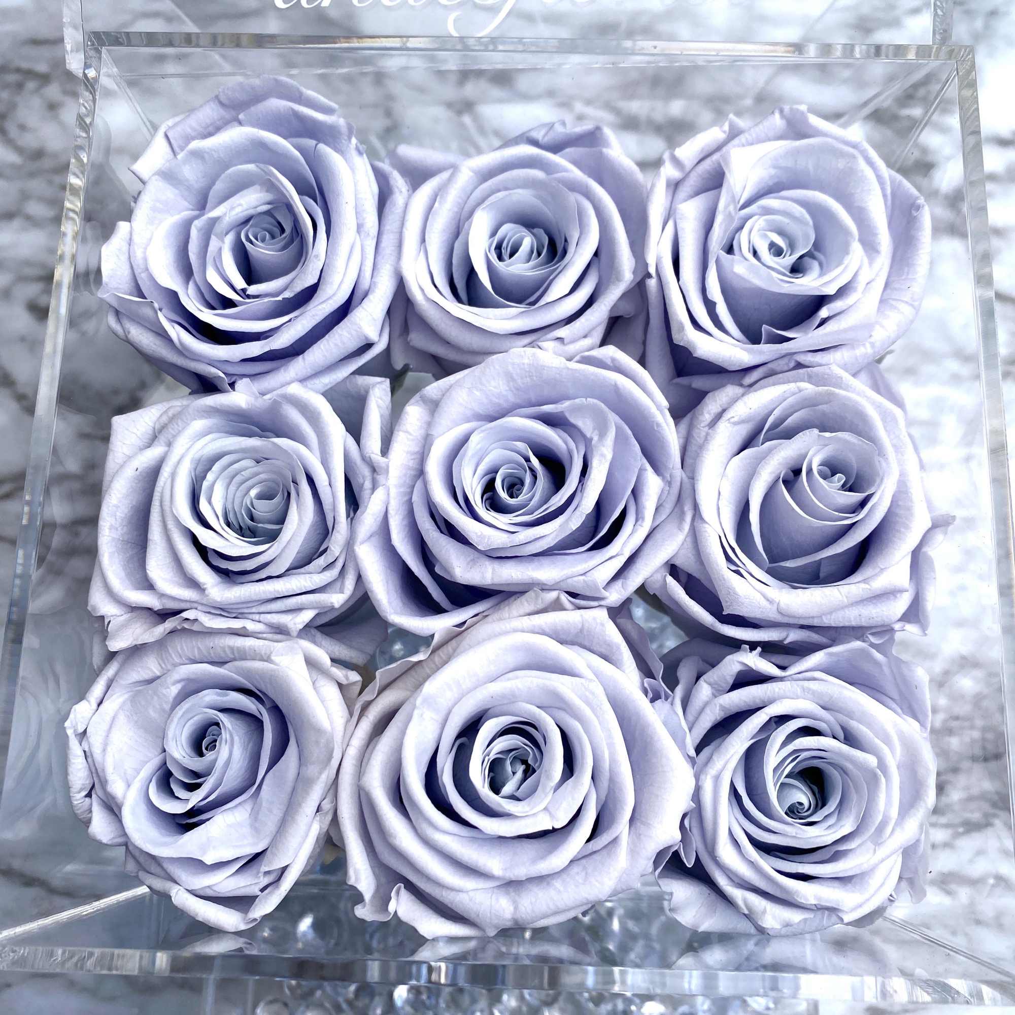 Nine pale lavender roses arranged in a clear acrylic box