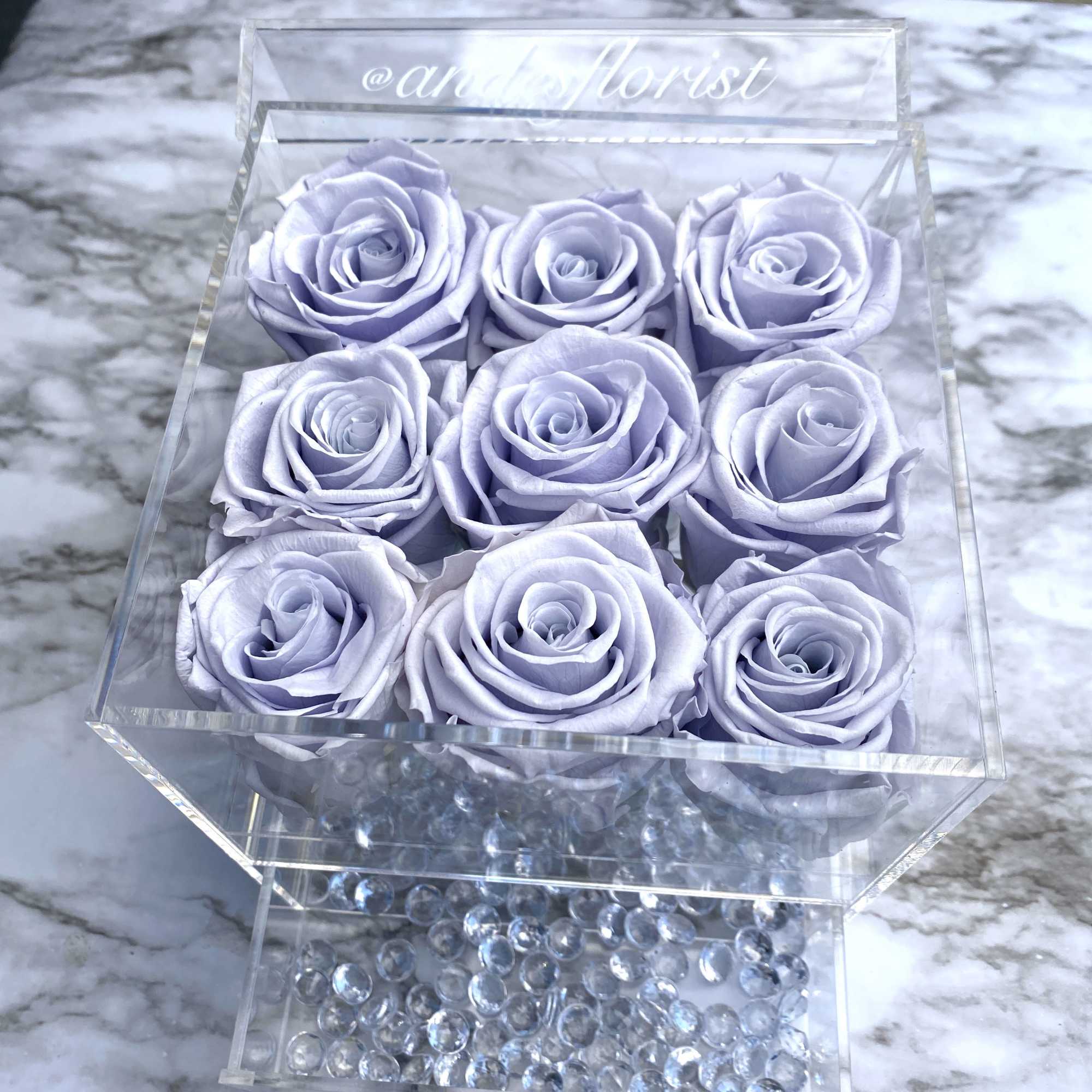 Lavender roses arranged in a clear acrylic box with decorative beads.
