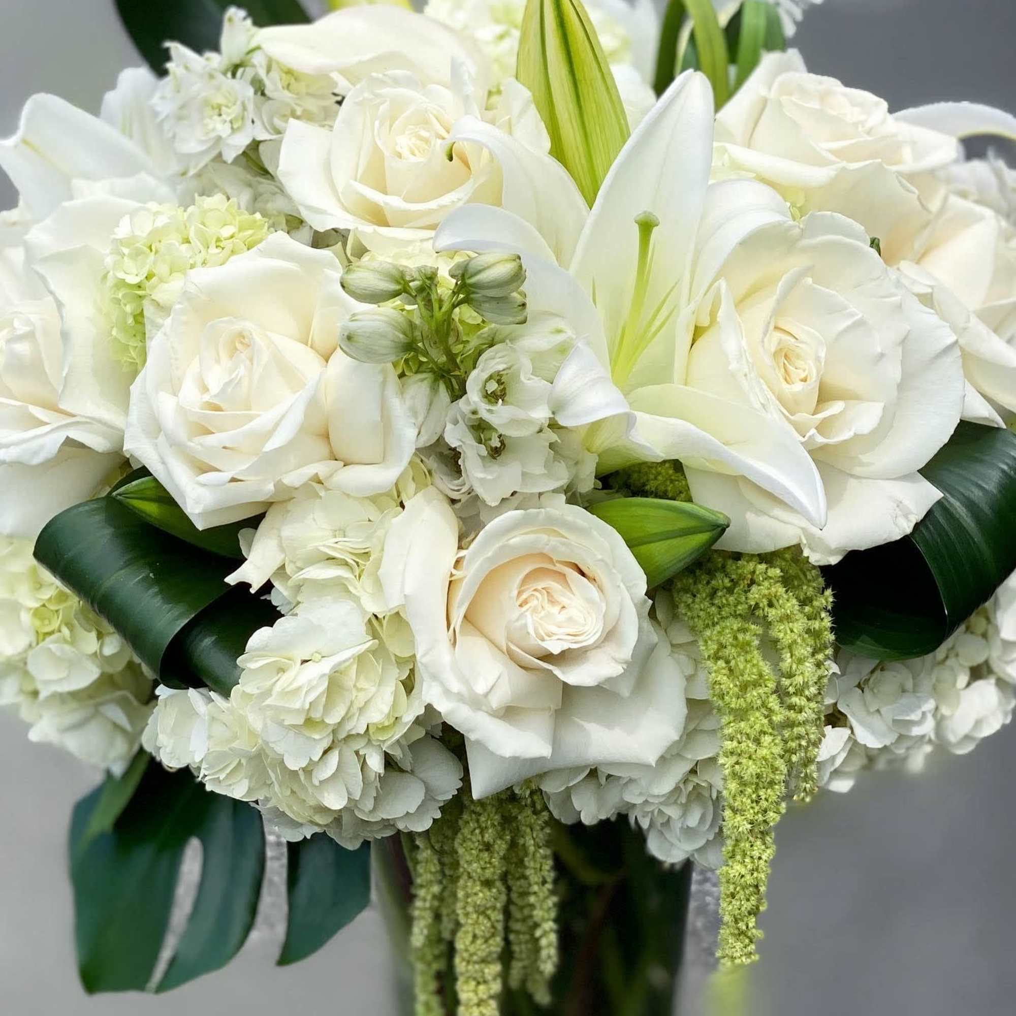 White roses and lilies arranged in a bouquet with dark green leaves.