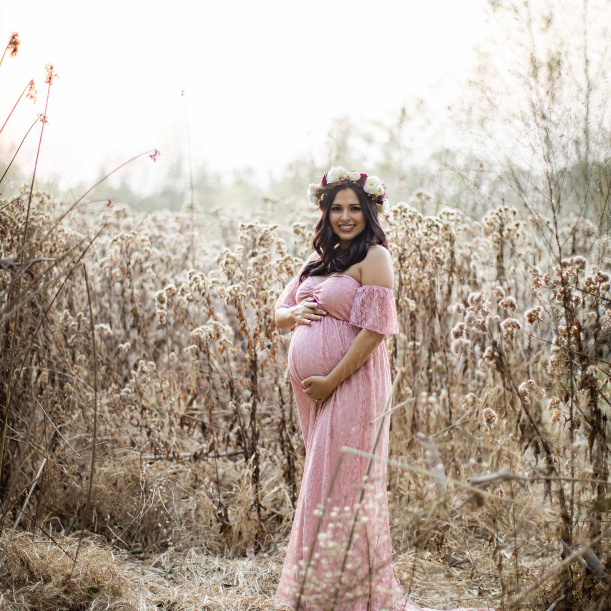 Pregnant woman in a pink dress wearing a flower crown in a field, photo 4 of 4