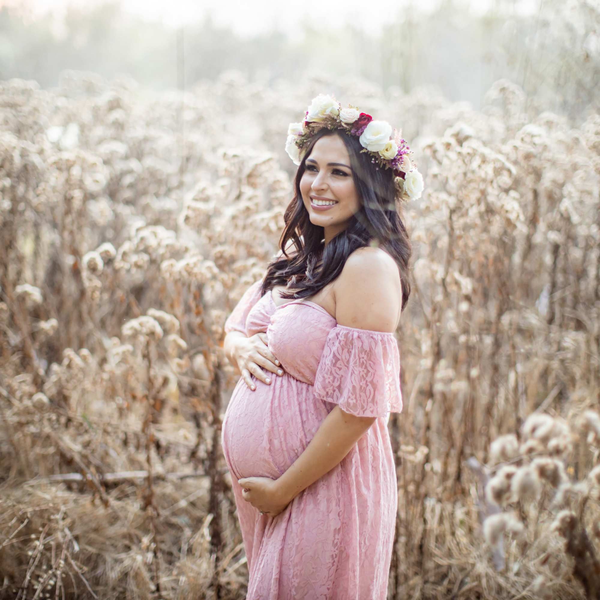 Pregnant woman in a pink dress wearing a flower crown in a field, photo 2 of 4