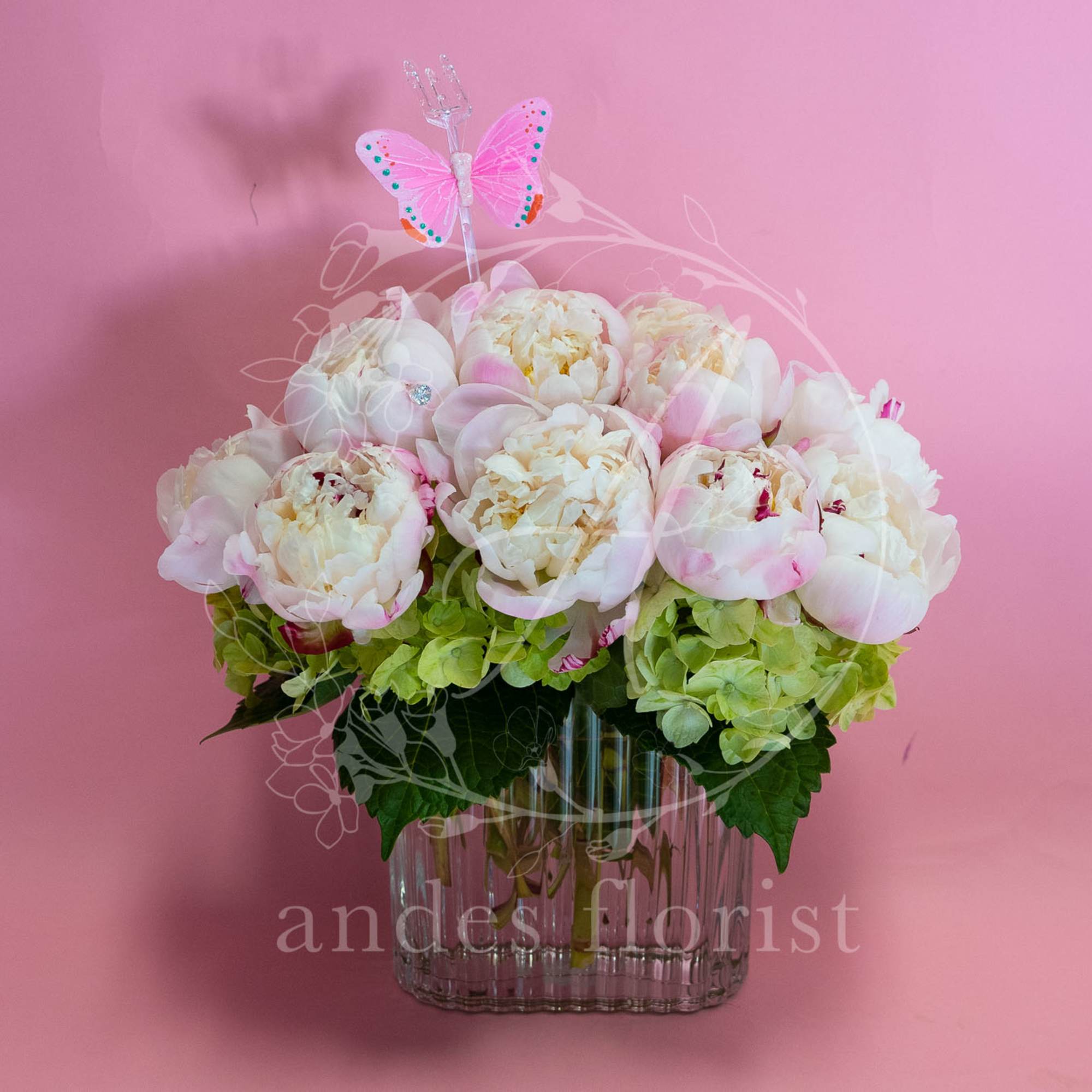 Pink and white peonies in a clear glass vase with a butterfly pick