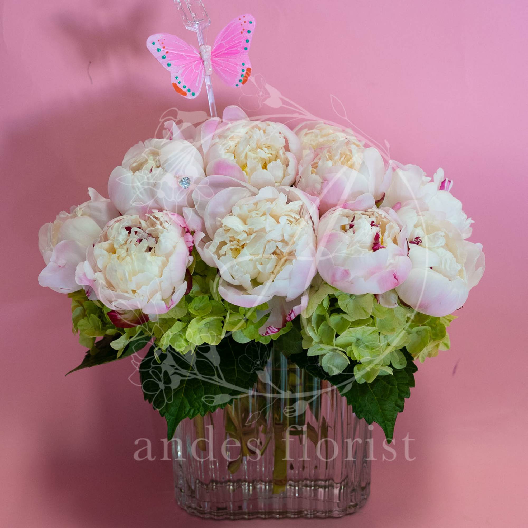 Pink and white peonies in a glass vase with a butterfly pick
