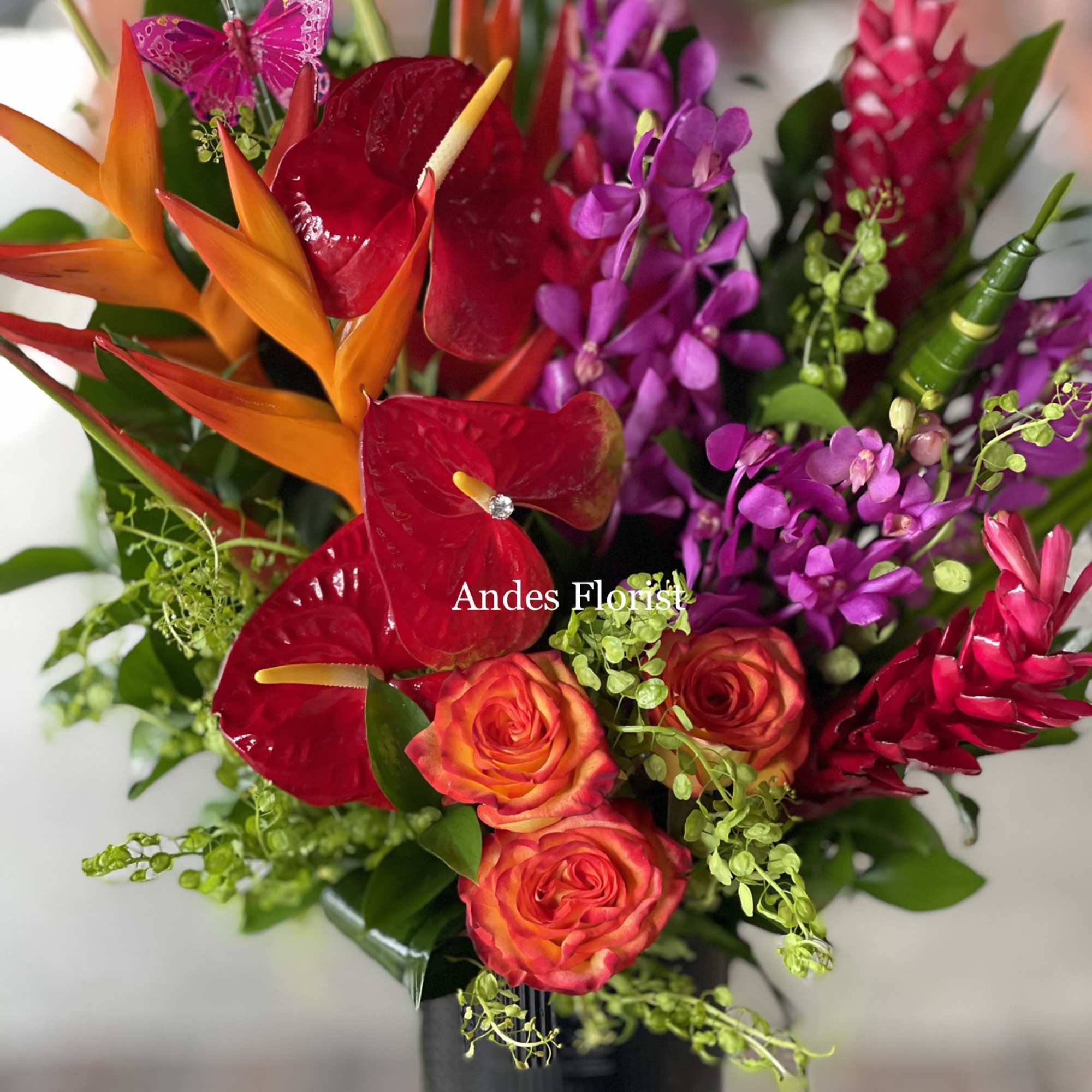 Tropical bouquet with red anthuriums, orange heliconia, and purple orchids in a black vase