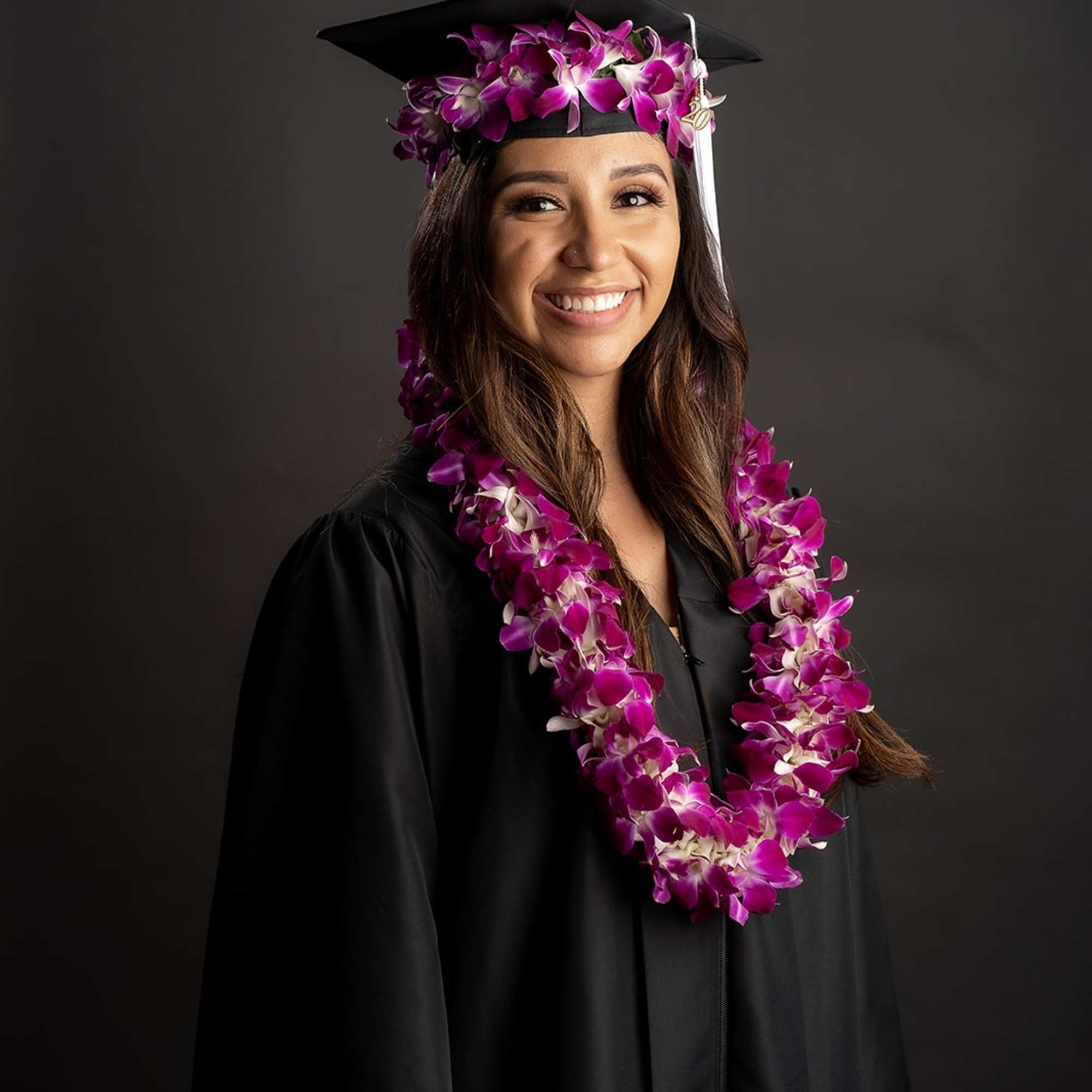 Graduate in a cap and gown wearing a purple orchid lei and matching cap flowers