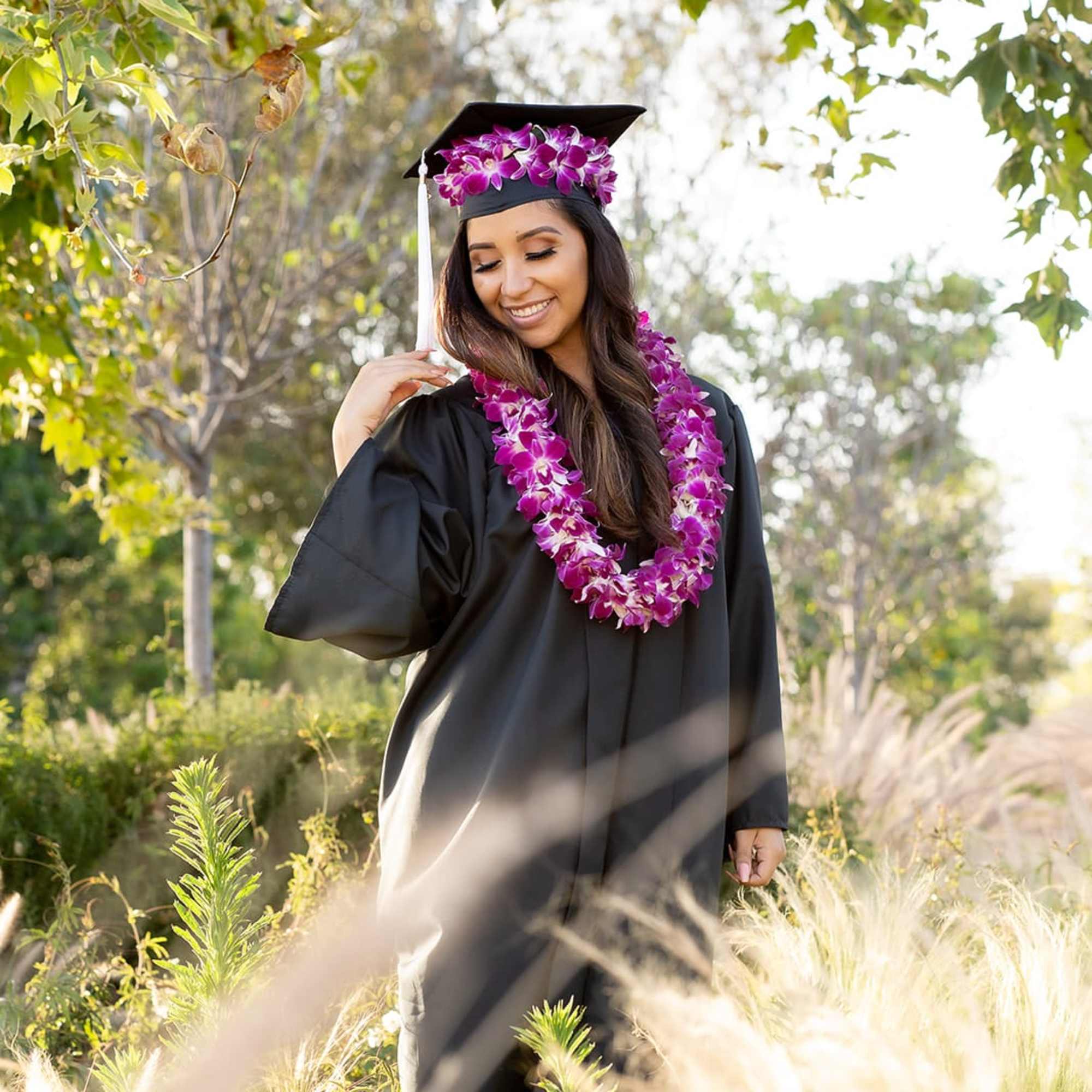 Graduate in a black cap and gown wearing a purple flower lei and cap decoration