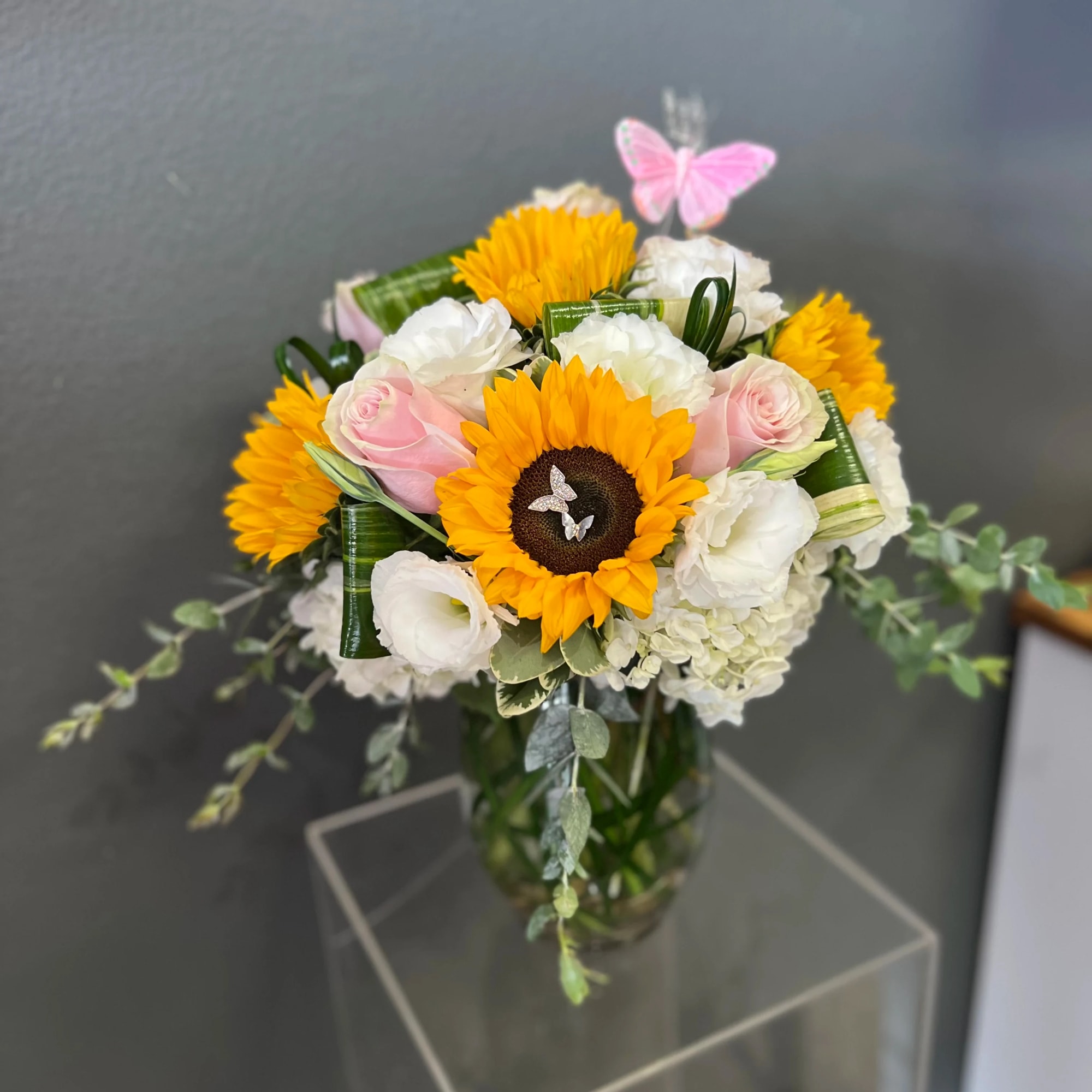 Bouquet of sunflowers, pink roses, and white blooms in a glass vase