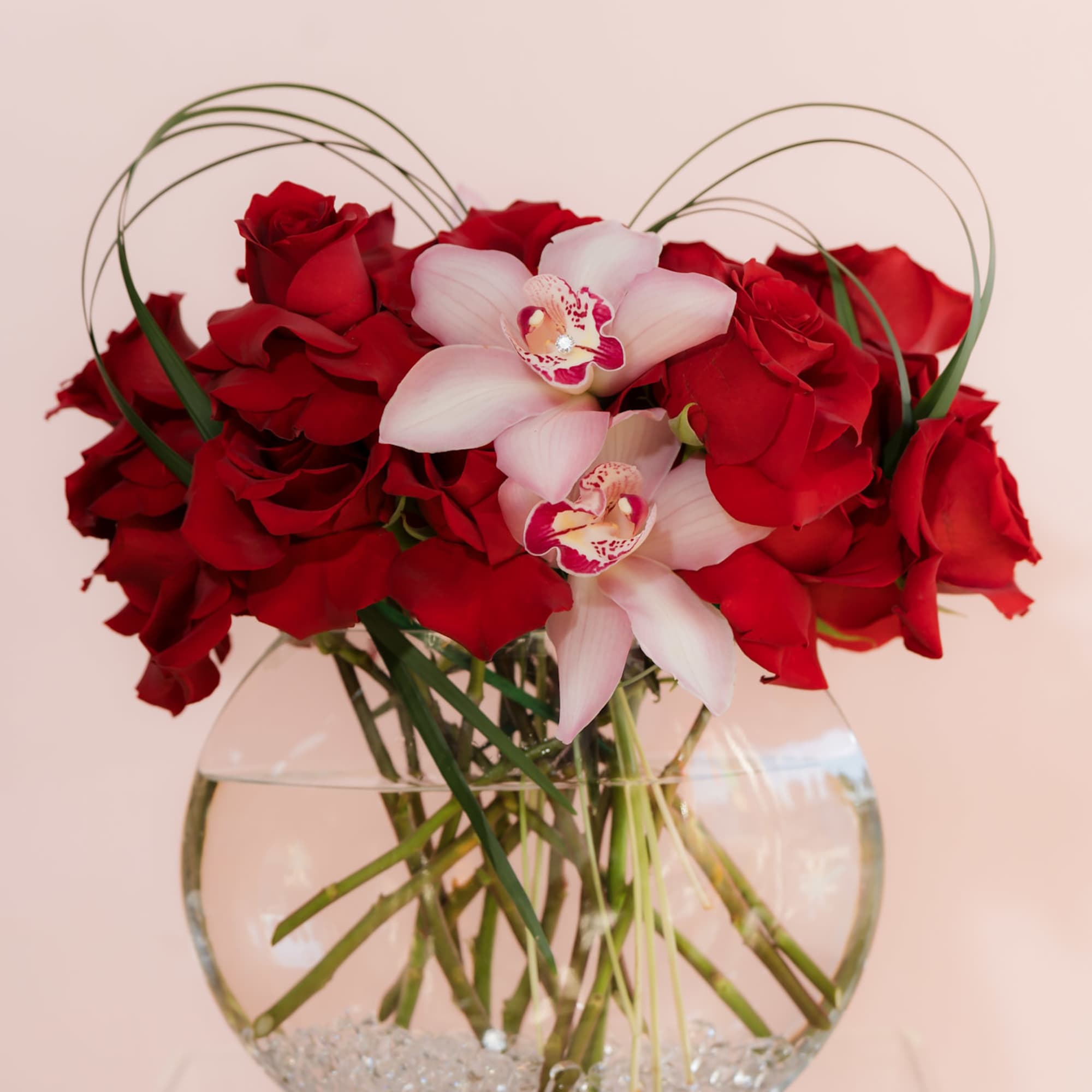 Red roses and pale pink orchids in a clear glass vase