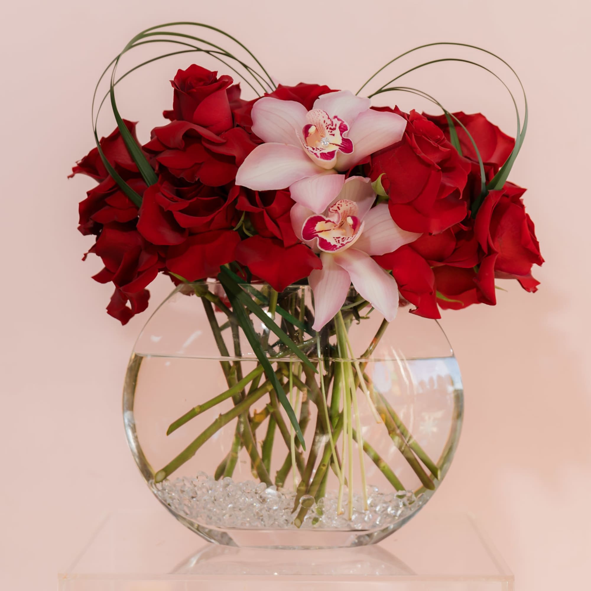 Red roses and pale orchids in a round glass vase