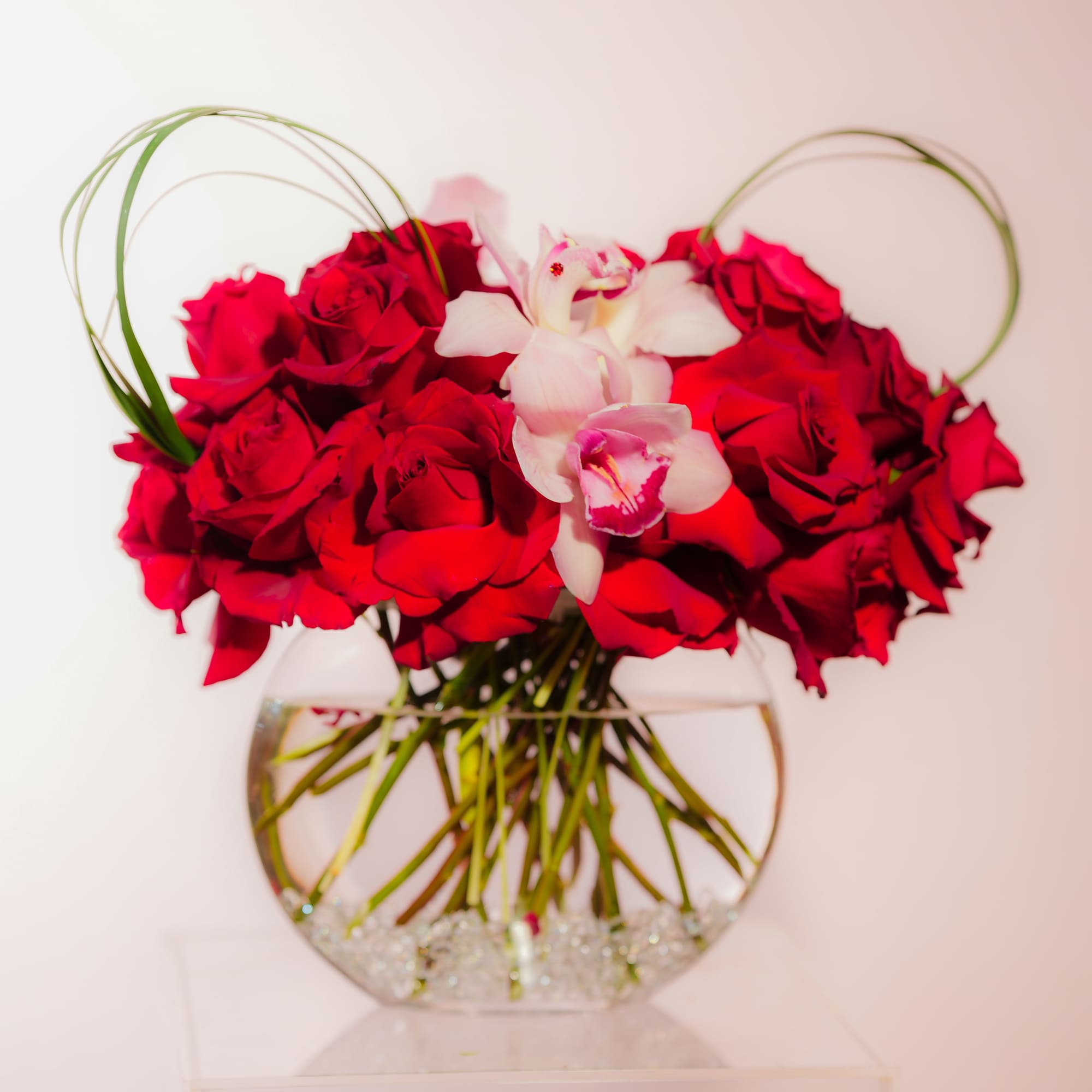Red roses and white orchids arranged in a round glass vase