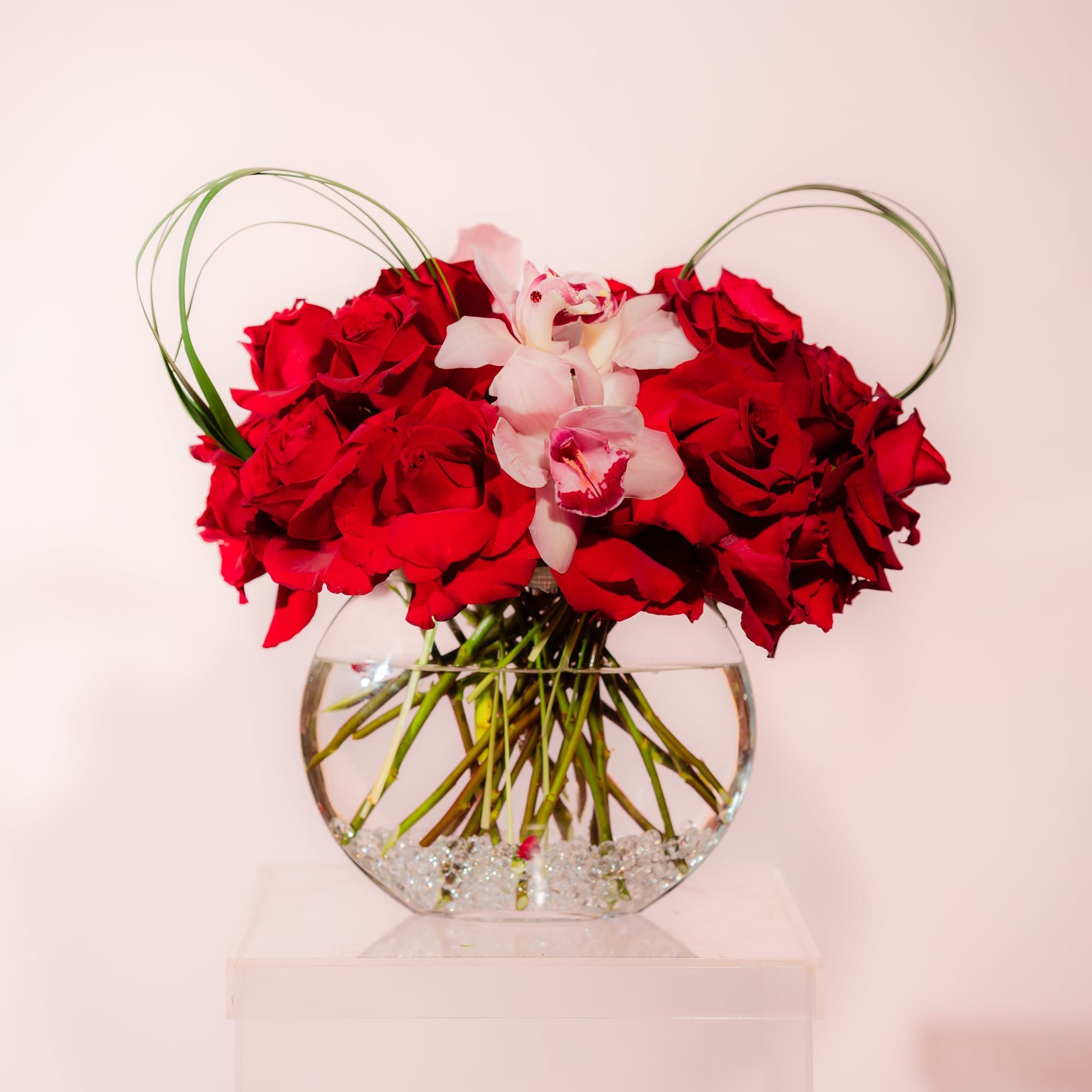 Red roses and pale pink orchids in a round glass vase