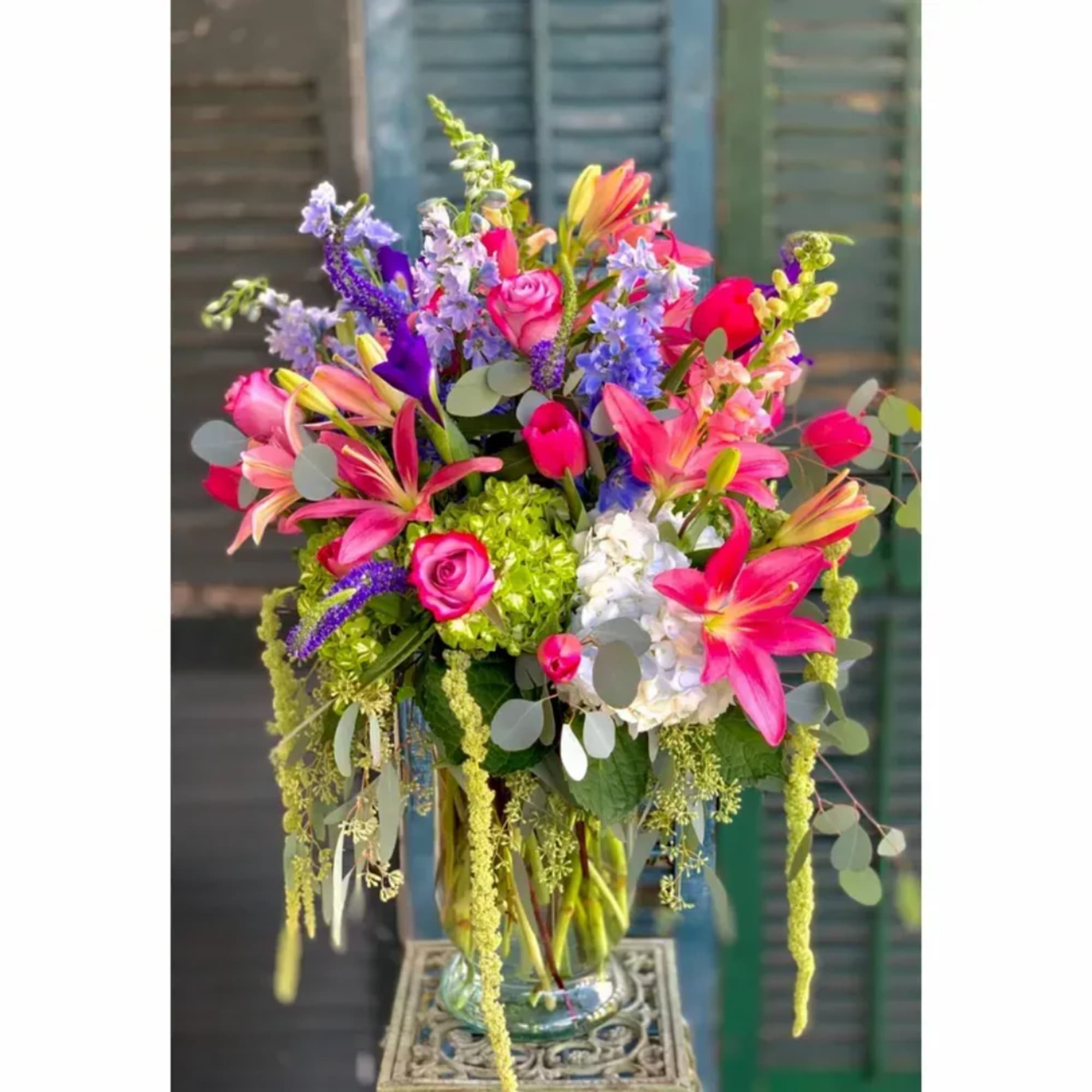 Bright mixed bouquet in a glass vase with pink lilies, roses, and blue flowers