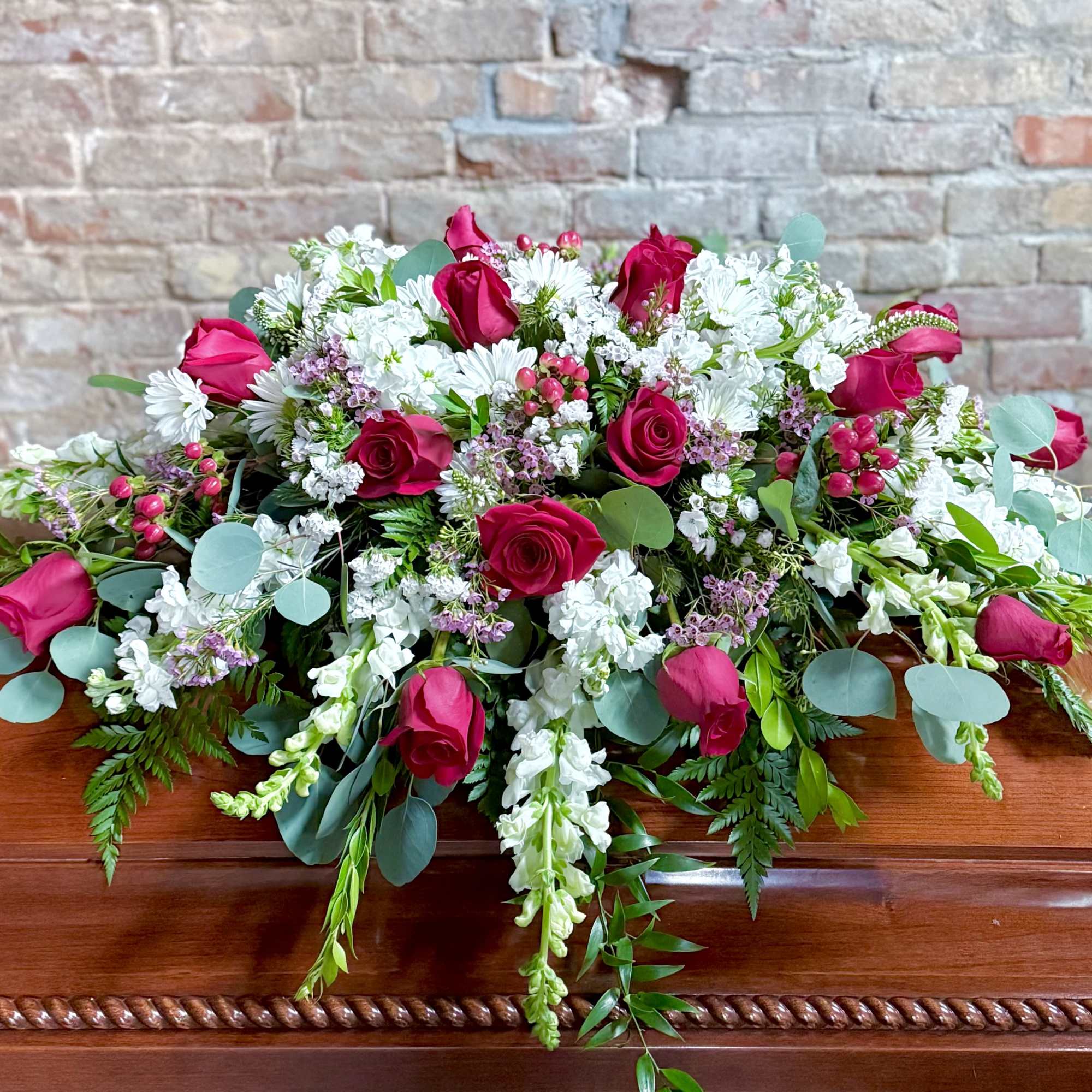 Casket spray with pink roses, white flowers, and greenery