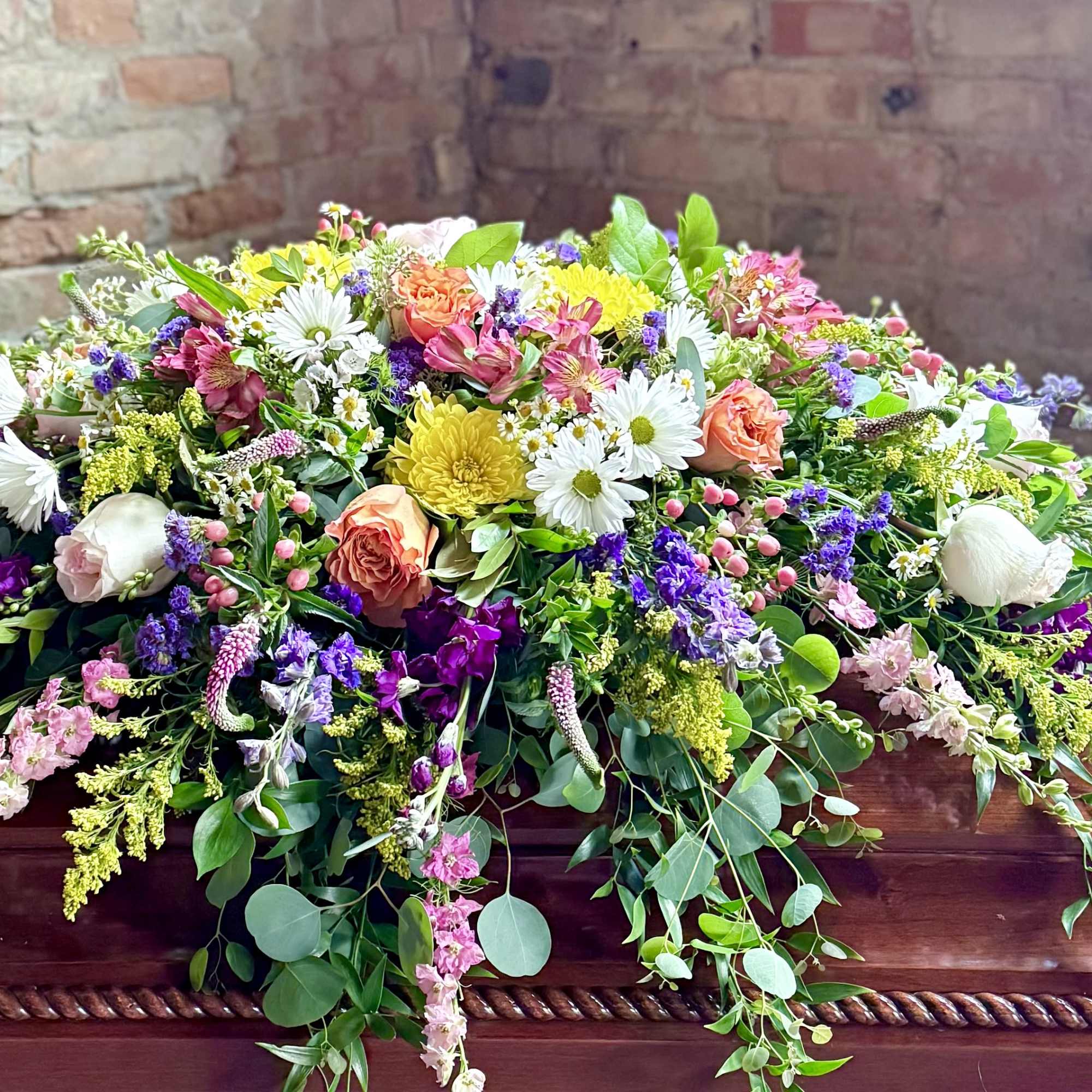 Large floral casket spray with mixed pink, white, yellow, and purple flowers