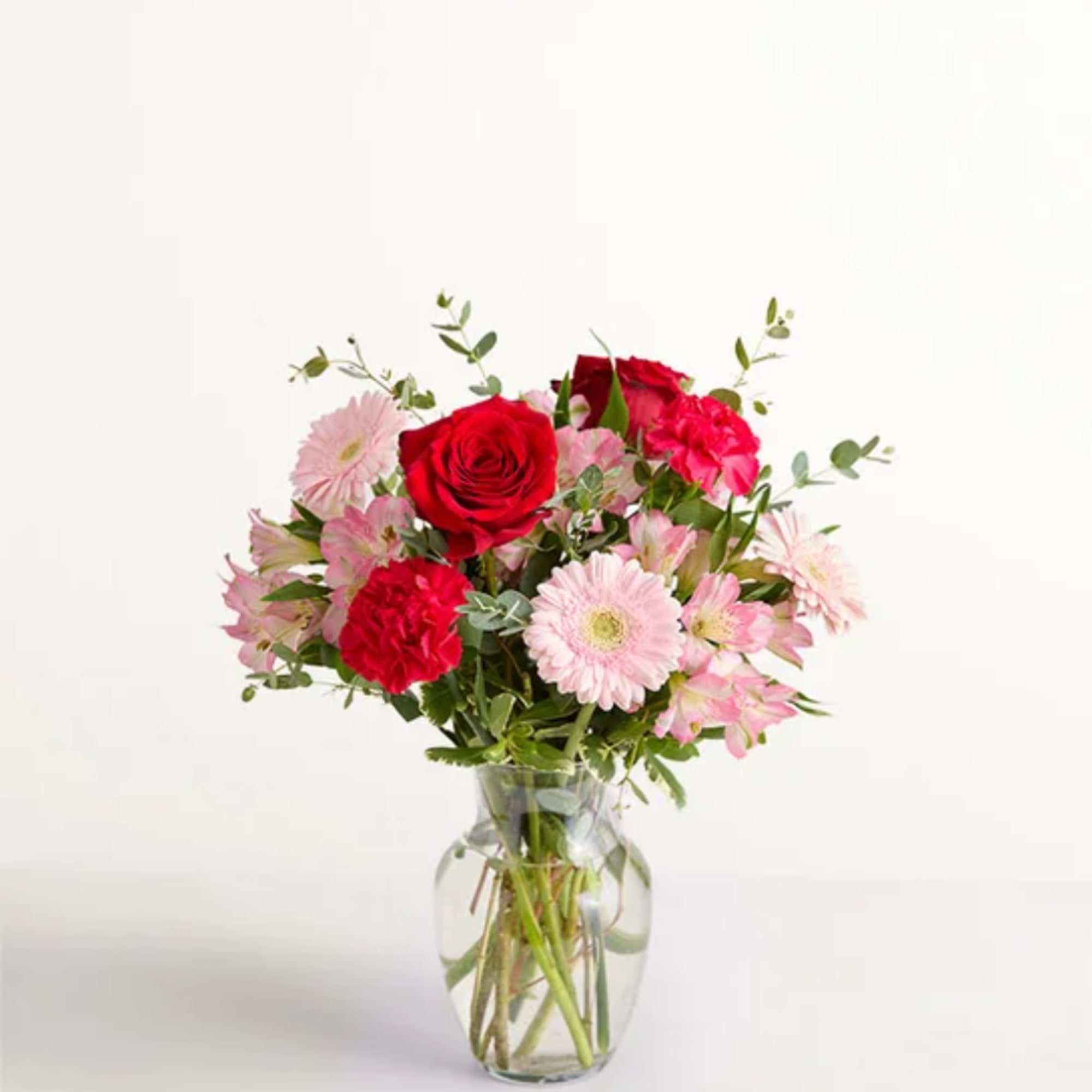 Pink and red mixed flowers arranged in a clear glass vase