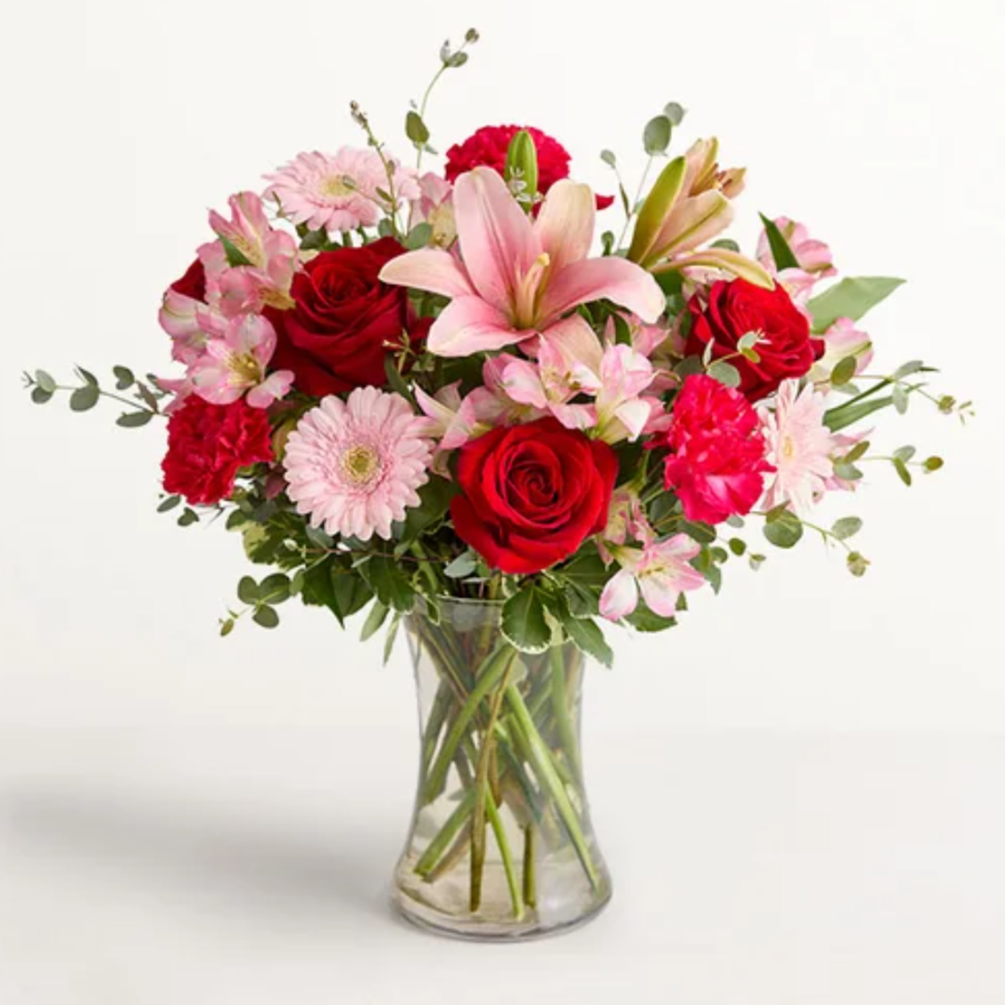 Mixed bouquet of red roses, pink lilies, and carnations in a glass vase