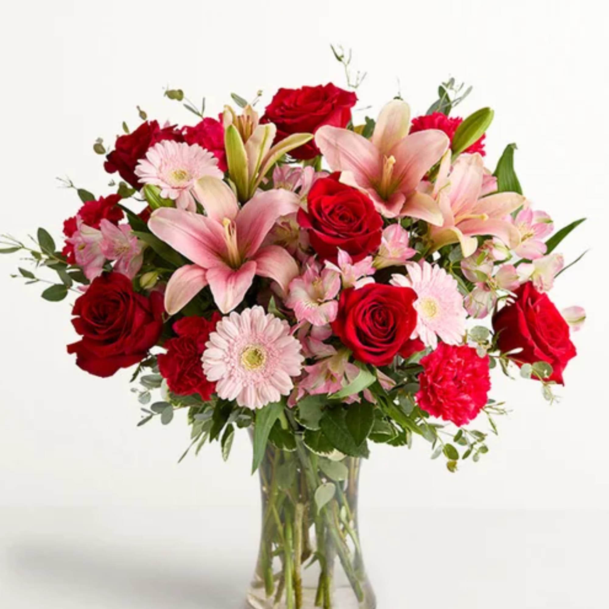 Mixed bouquet of red roses, pink lilies, and pale daisies in a clear glass vase