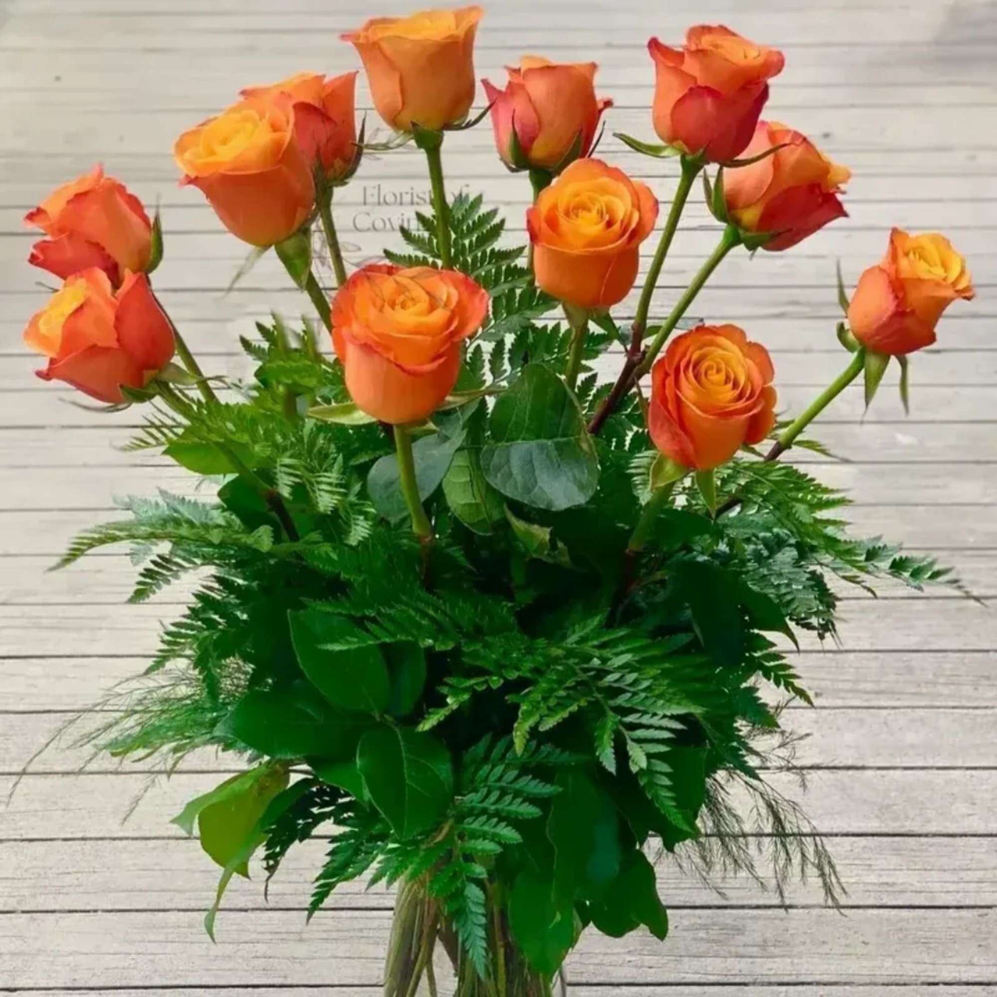 Orange roses arranged in a clear vase with dense greenery