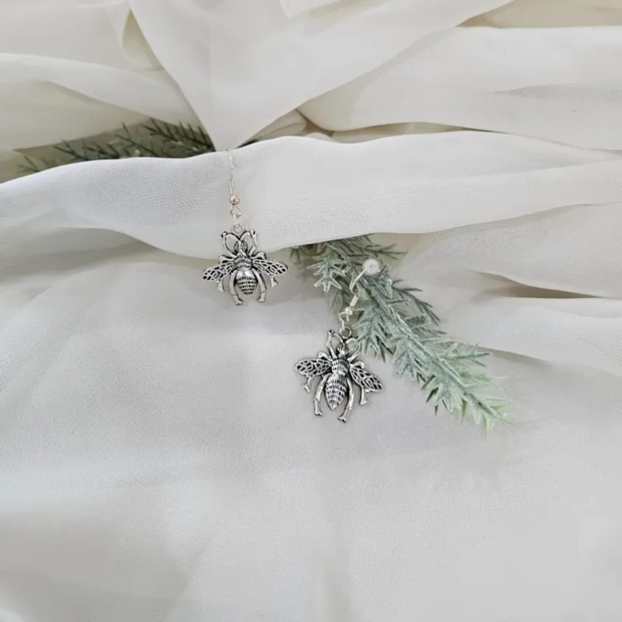 Bee-shaped earrings on white fabric with faux greenery