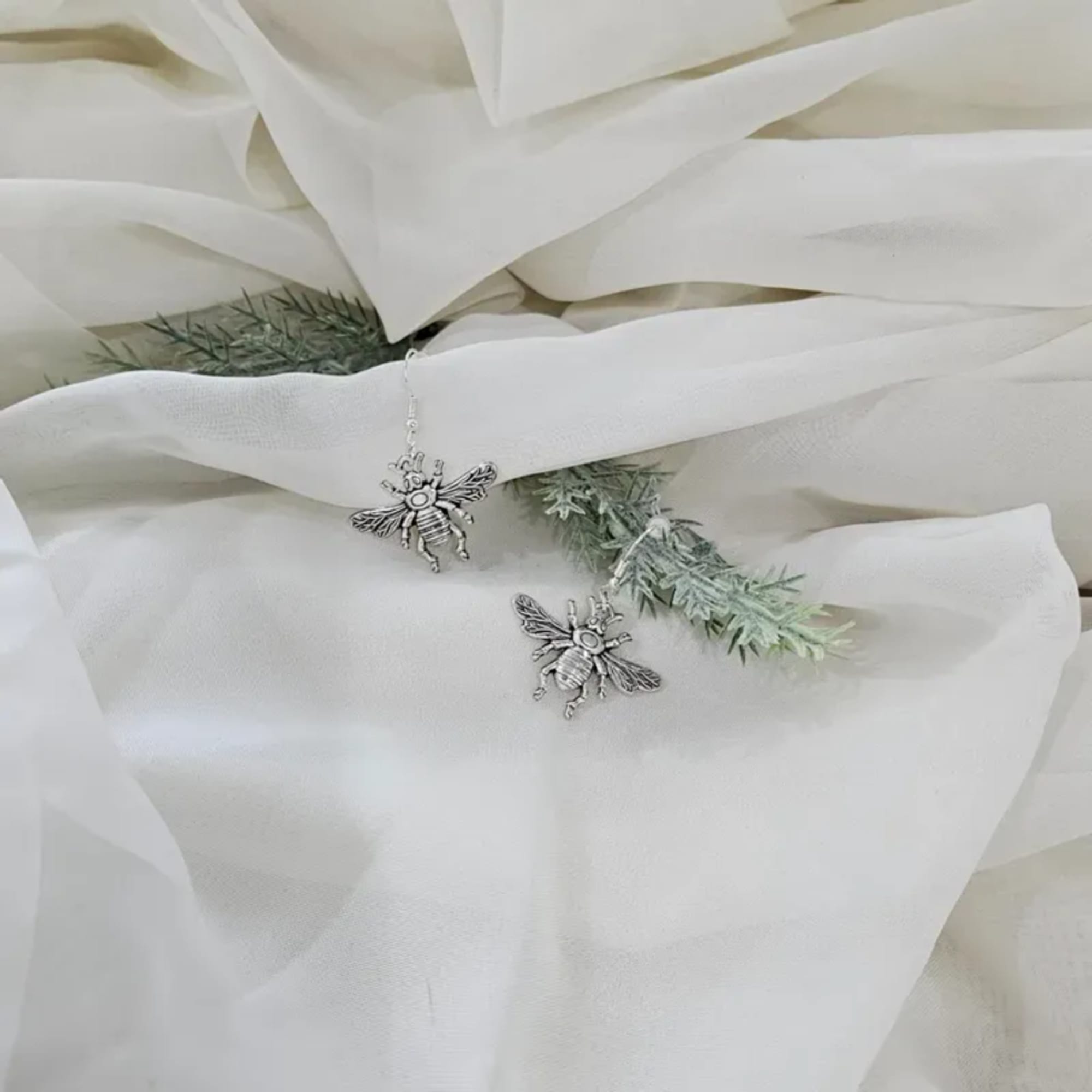 White fabric with small bee charms and sprigs of greenery