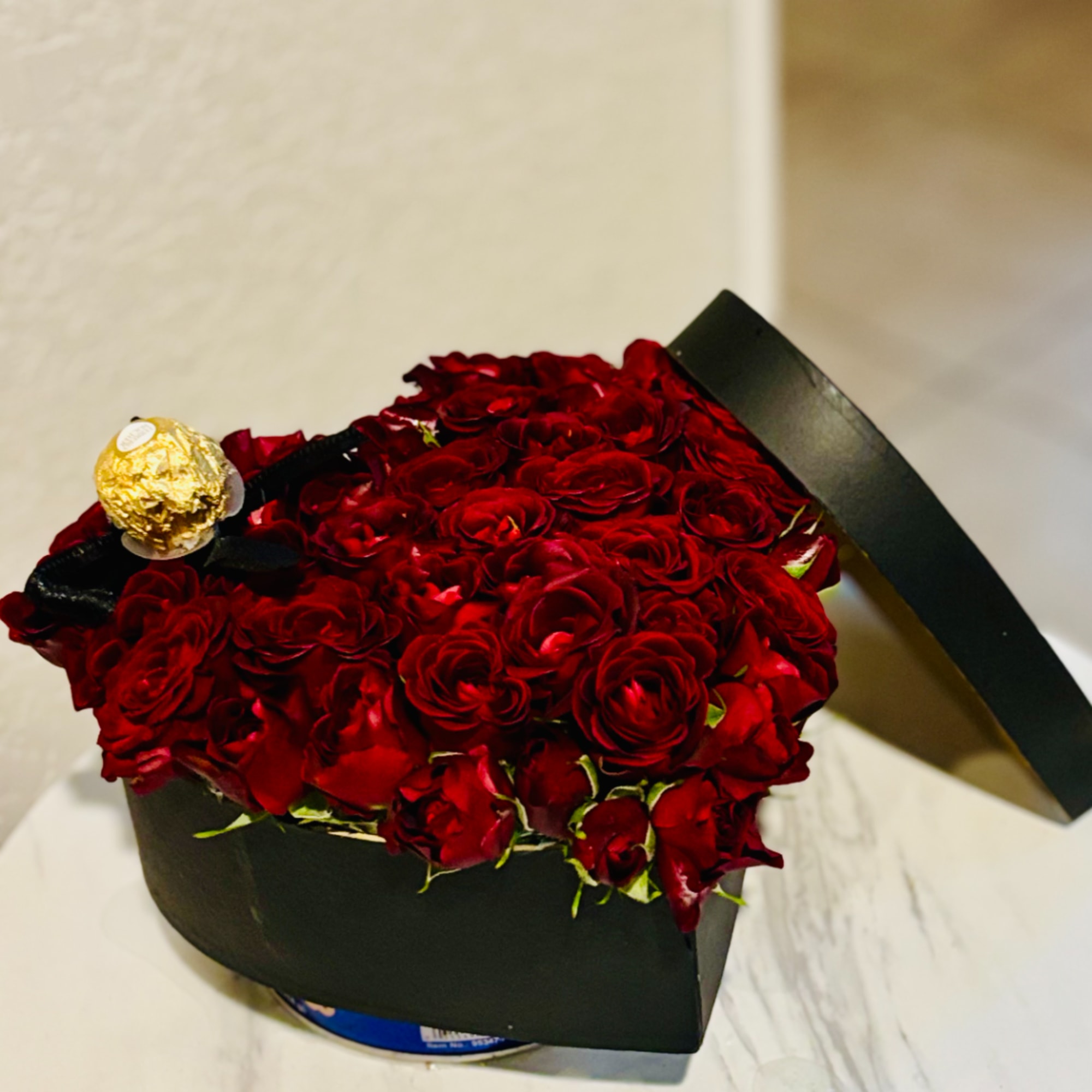Red roses arranged in a black box with a gold-wrapped chocolate