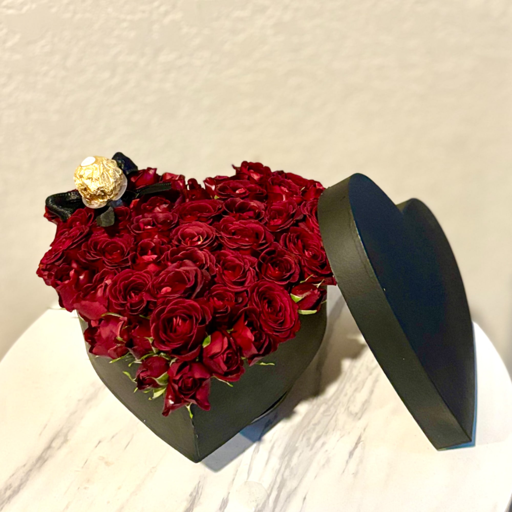 Heart-shaped box filled with red roses and a gold-wrapped chocolate