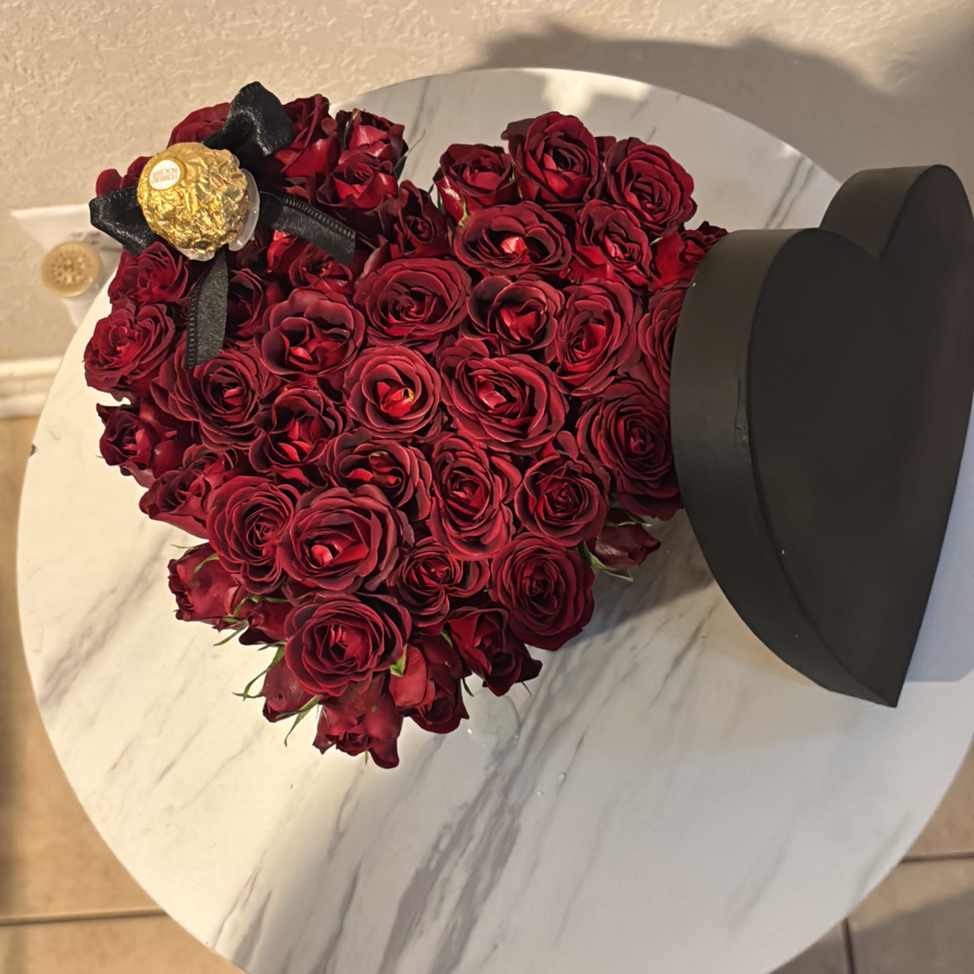 Heart-shaped bouquet of red roses in a black hat box with a gold candy topper