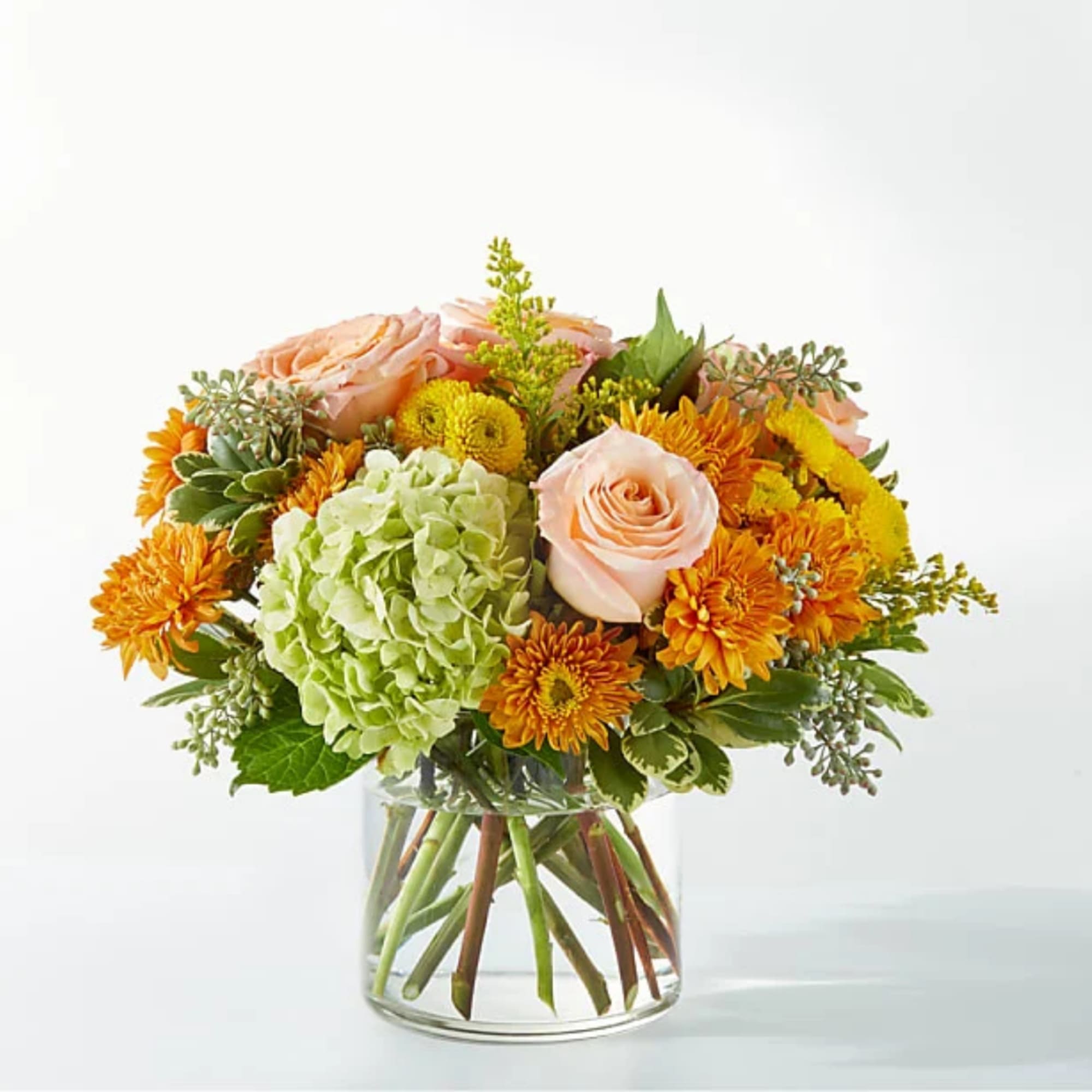 Mixed bouquet of peach roses, green hydrangea, and orange mums in a glass vase