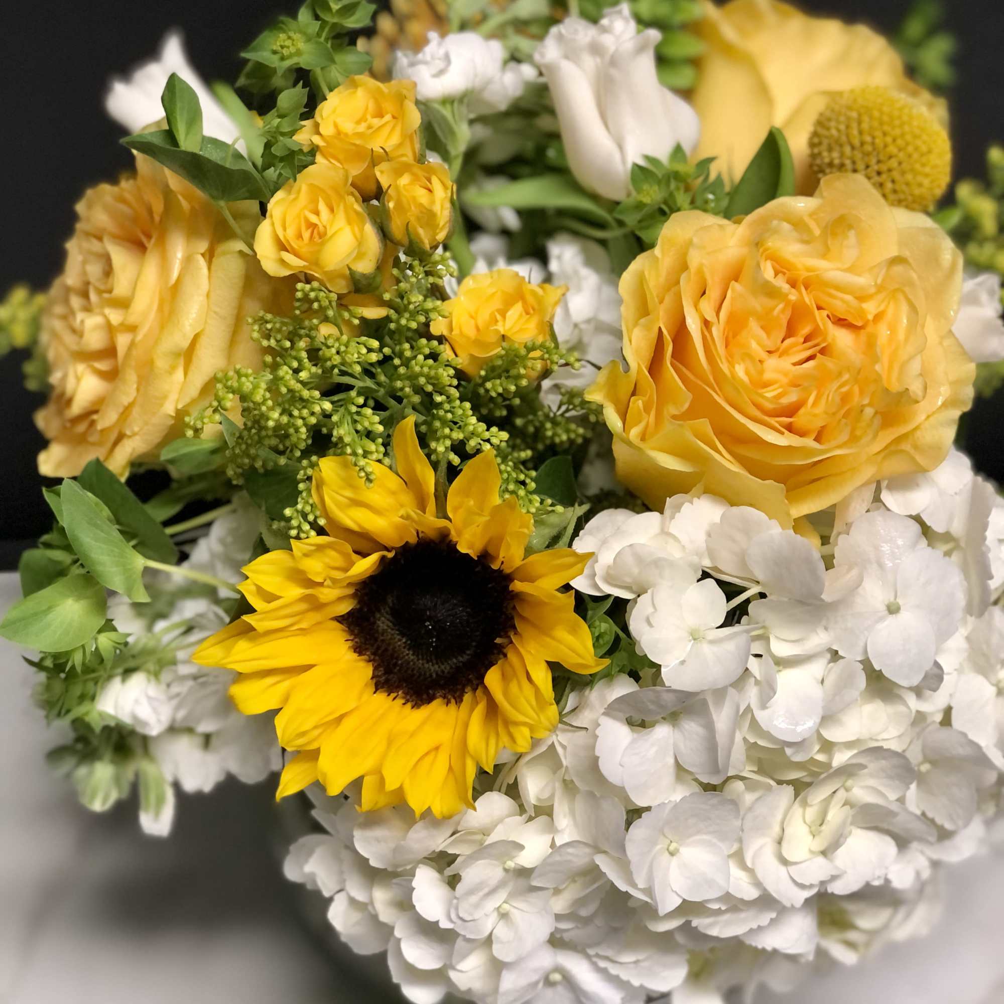 Yellow roses and a sunflower with white hydrangeas in a bouquet
