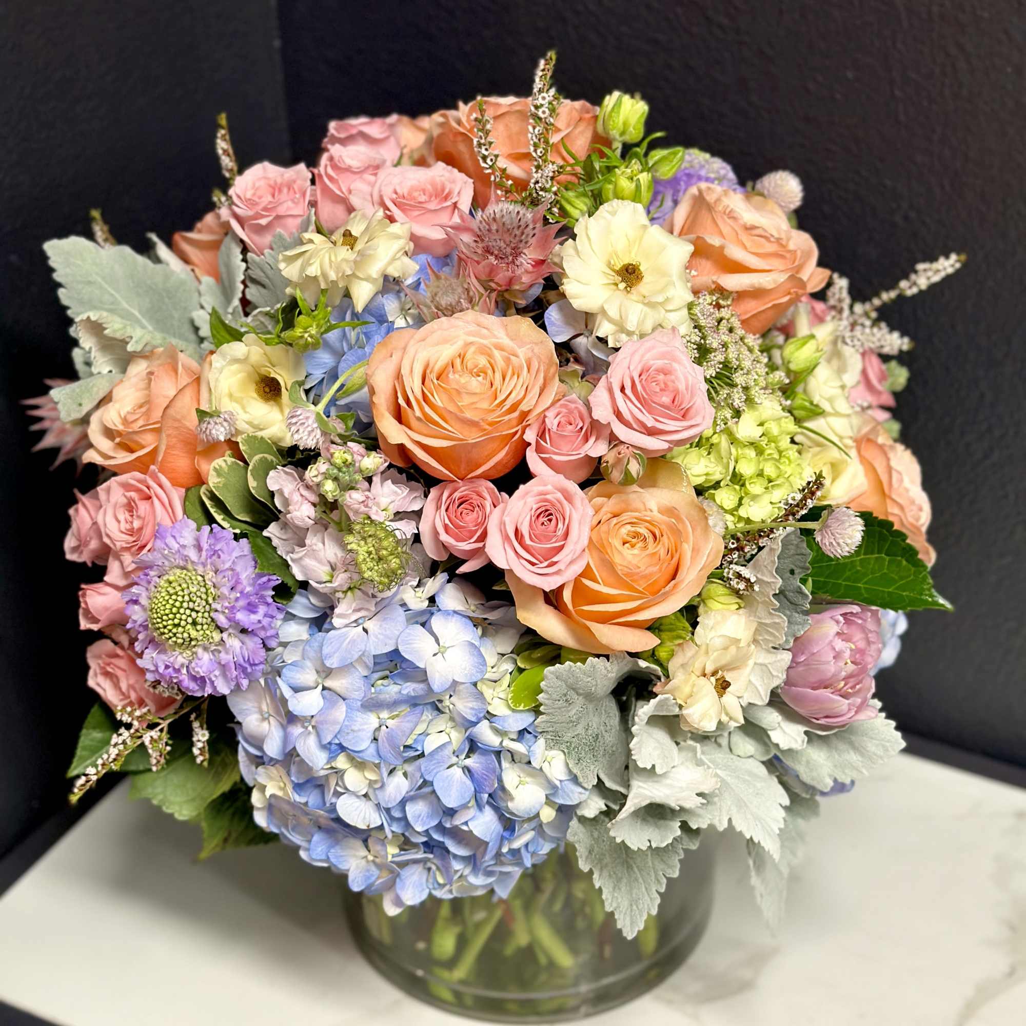 Mixed pastel bouquet of roses, hydrangeas, and daisies in a glass vase
