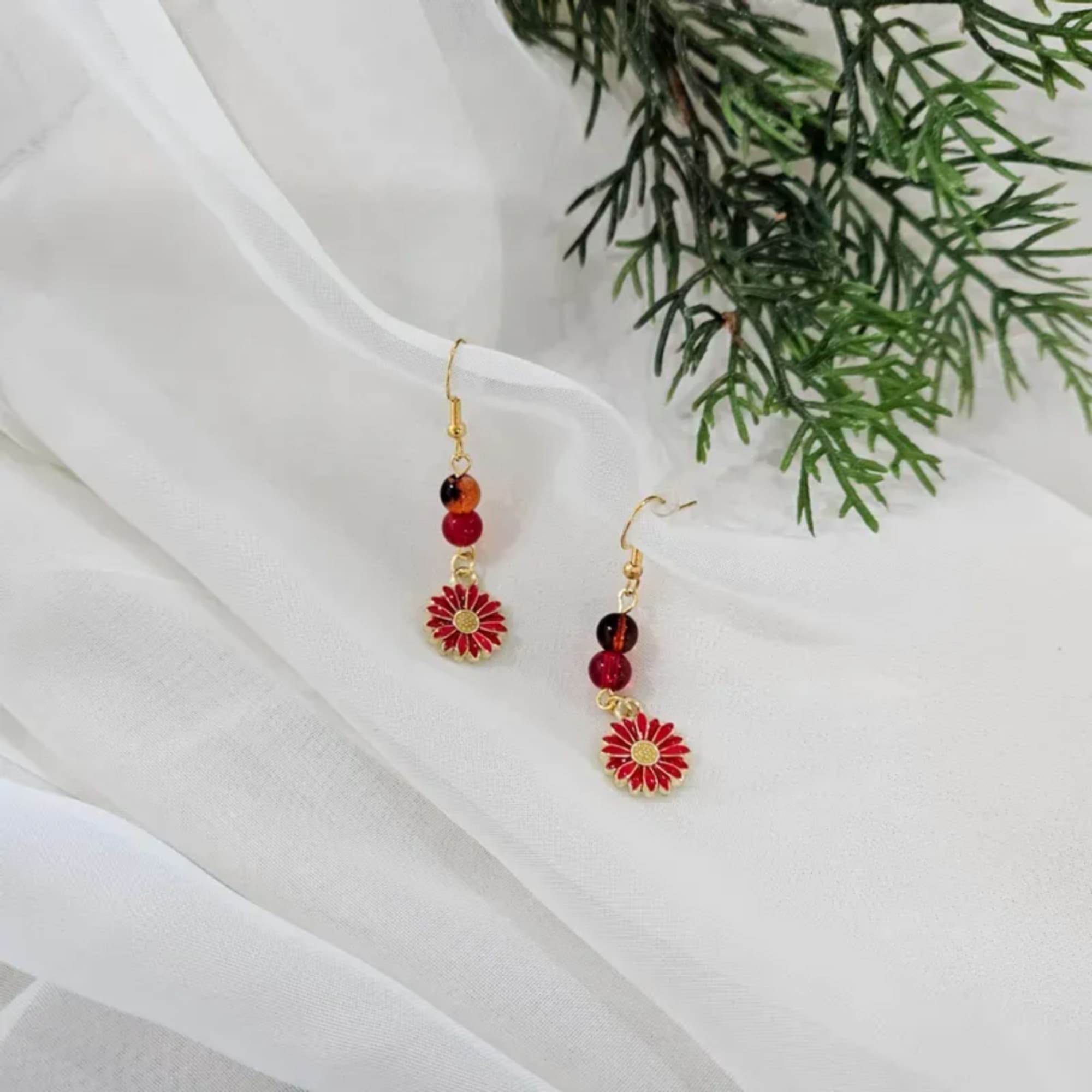 Pair of red floral drop earrings on white fabric