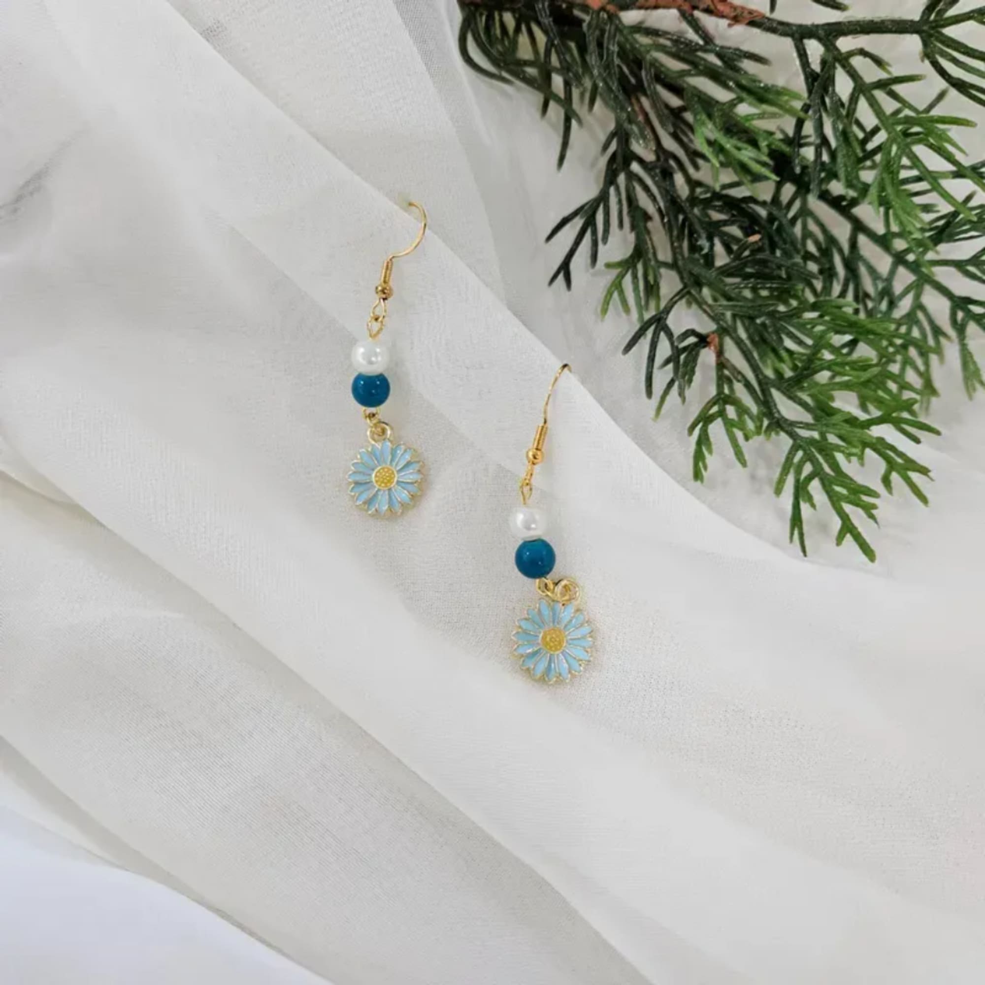 Pair of daisy drop earrings on white fabric with greenery