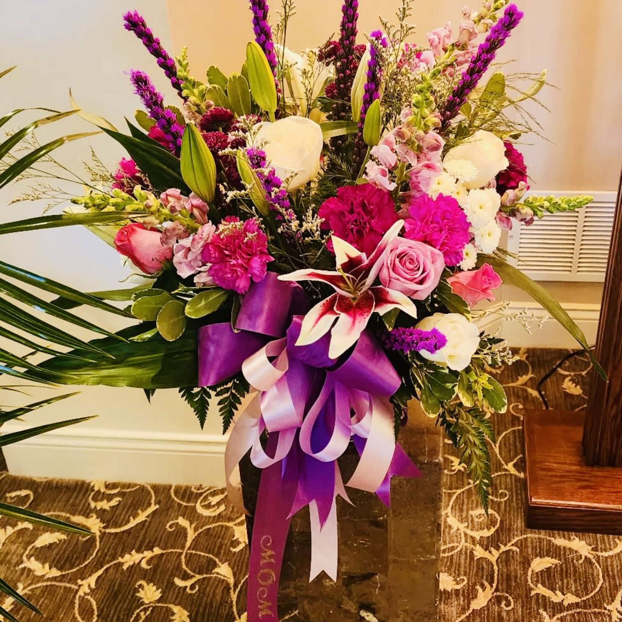 Tall bouquet of pink, white, and purple flowers in a dark vase with ribbon
