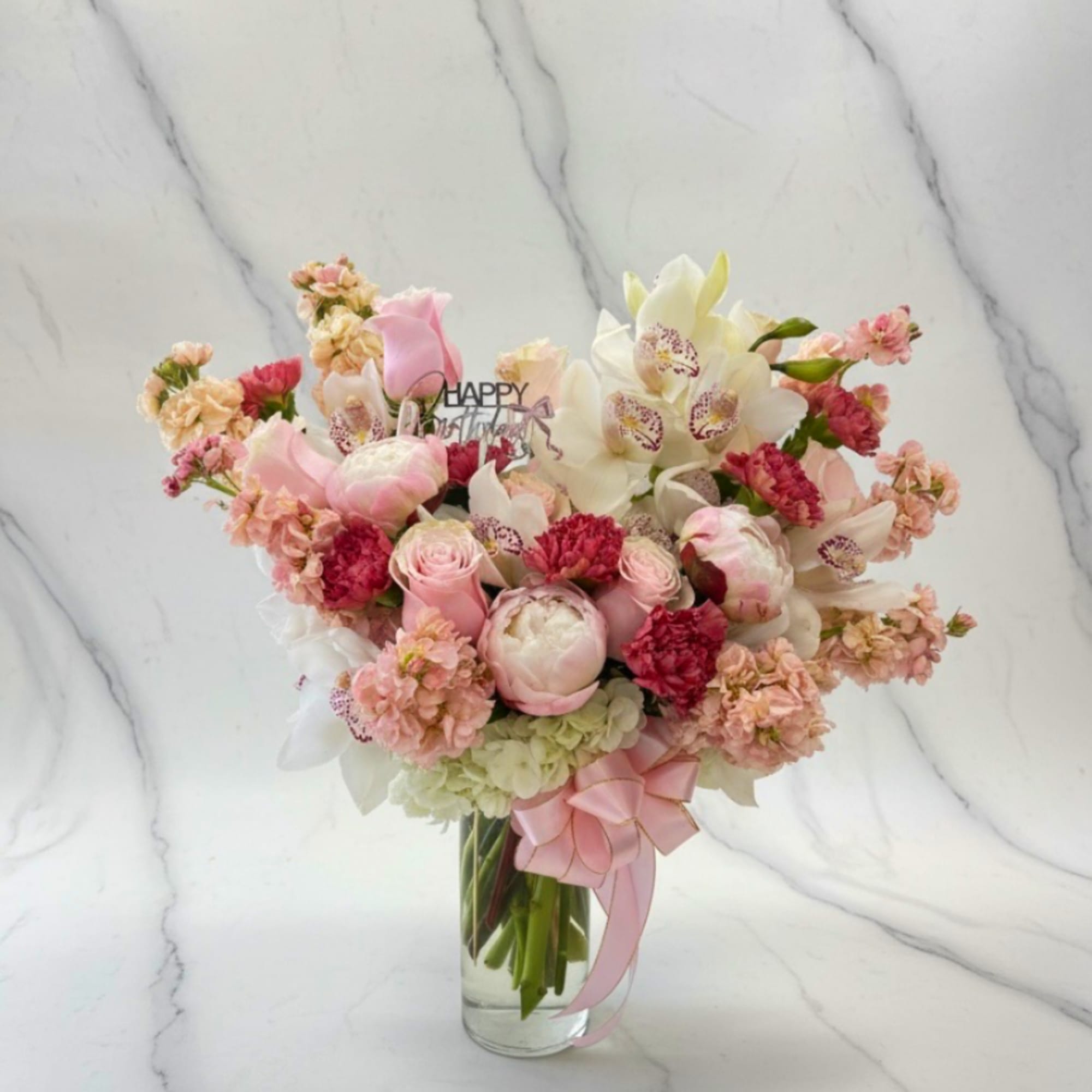Pink and white mixed flower bouquet in a clear glass vase with a pink ribbon