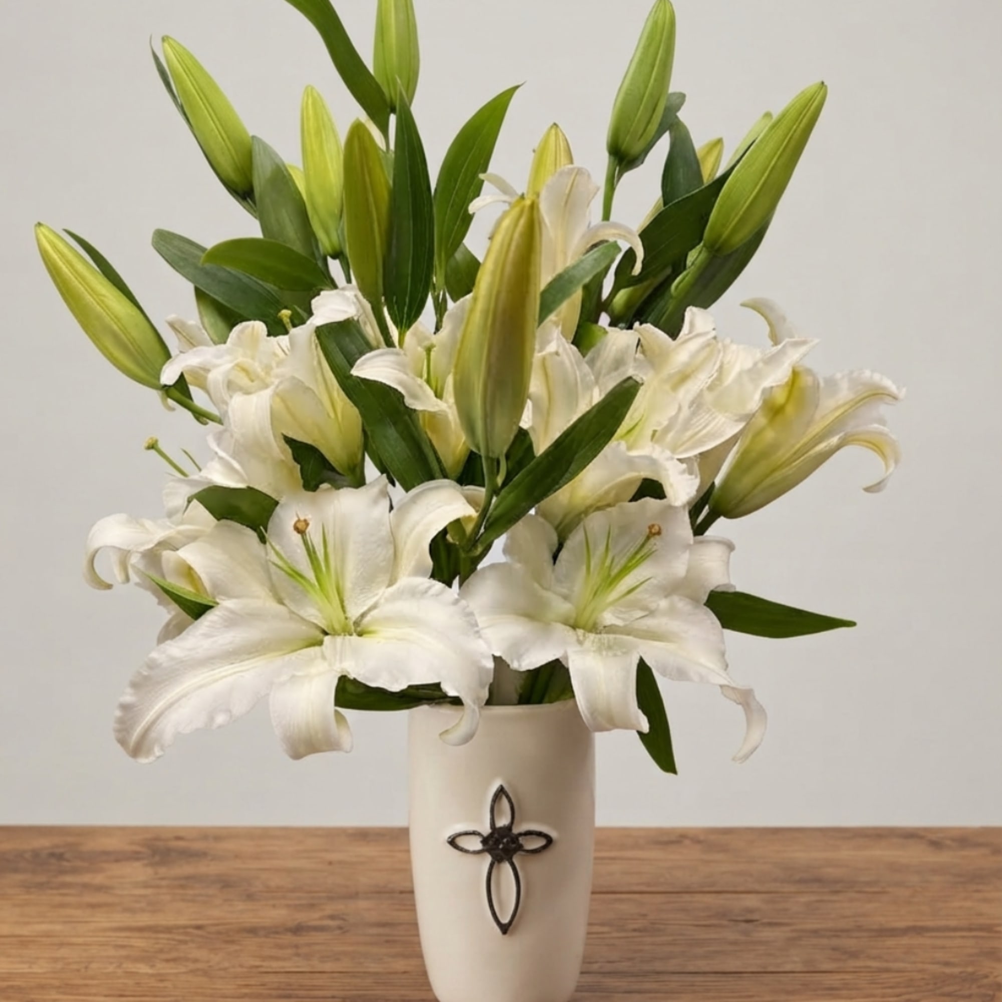 White lilies arranged in a cream vase on a wooden table