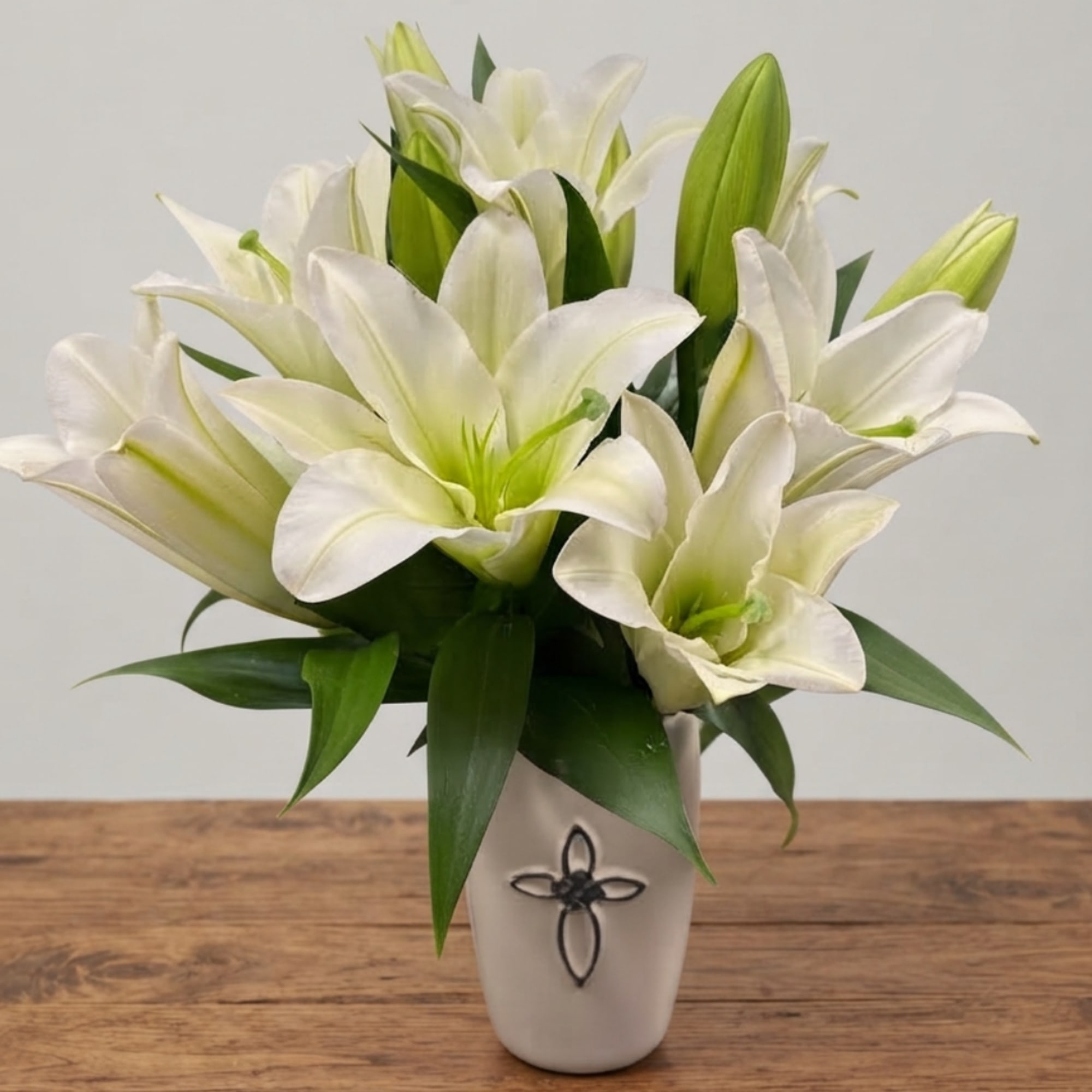 White lilies arranged in a white vase on a wooden table