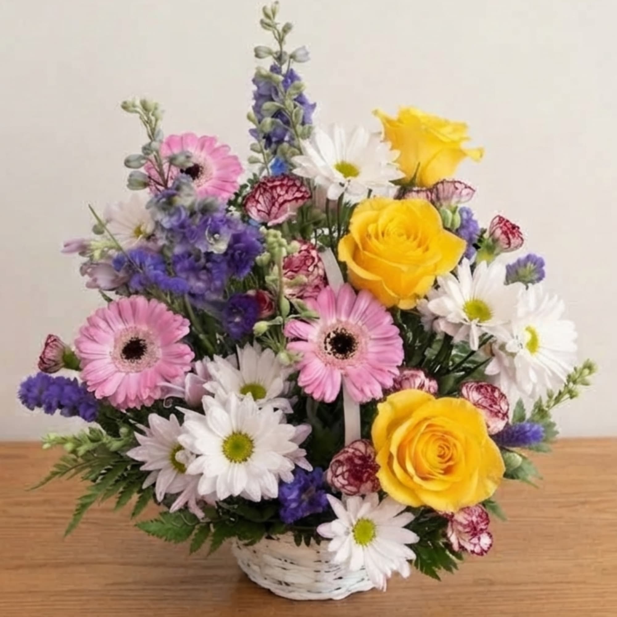 Mixed bouquet of yellow roses, pink gerberas, and white daisies in a white basket