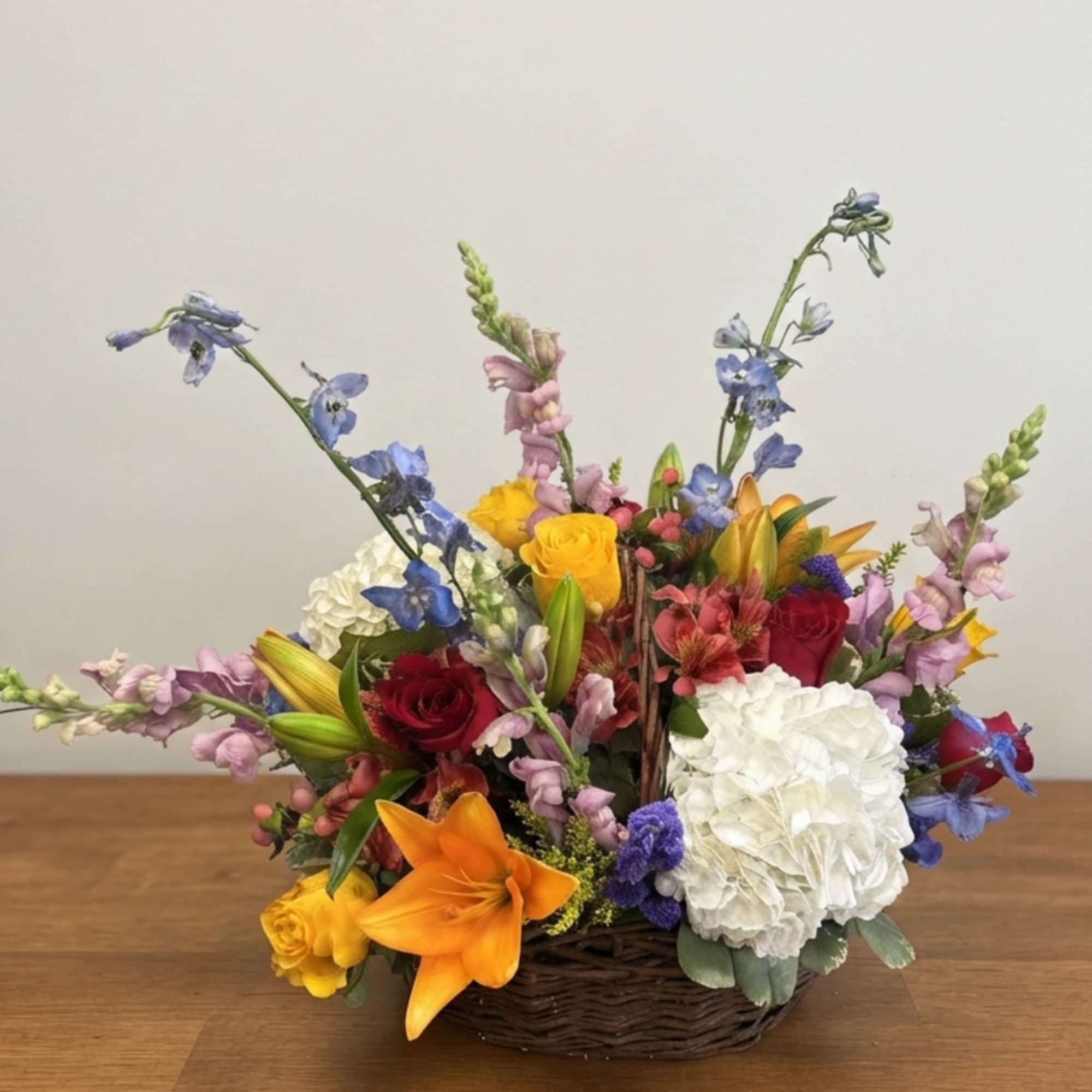 Colorful mixed flower arrangement in a wicker basket with lilies, roses, and hydrangeas