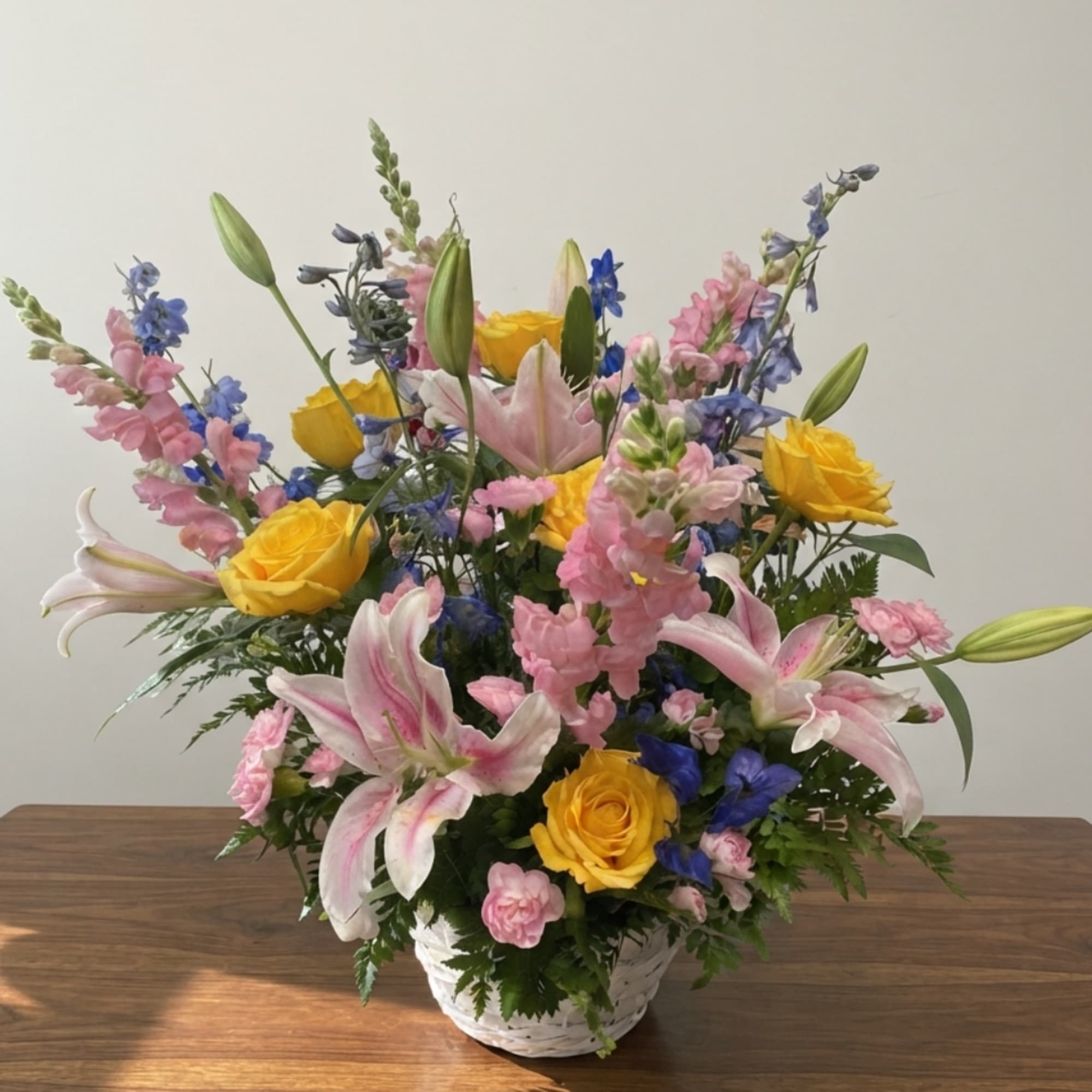 Mixed bouquet in a white basket with pink lilies, yellow roses, and blue flowers